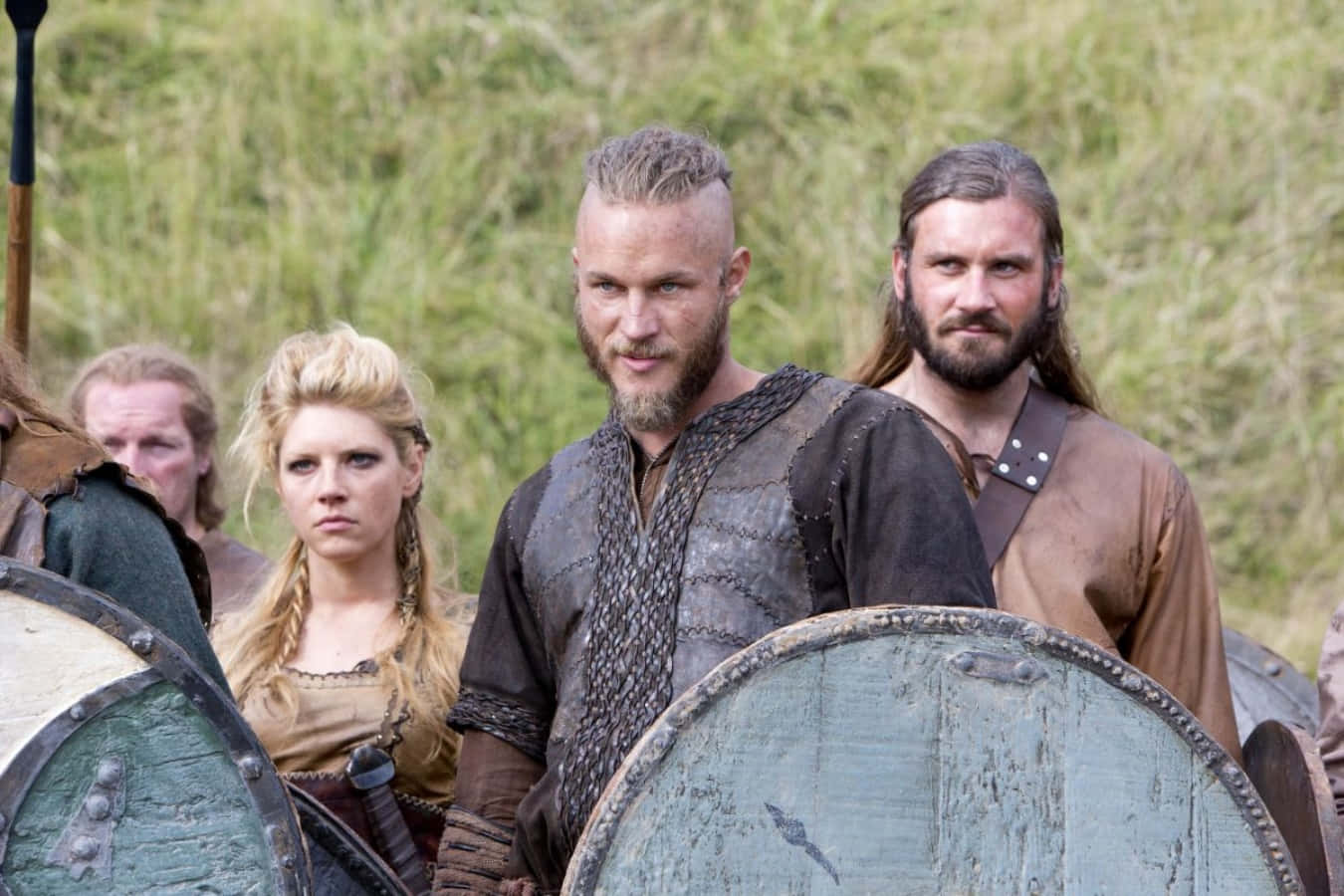 Vikings 桌布 壁紙 — 維京戰士們編著辮子、手持盾牌，神情嚴肅地站在草地上。