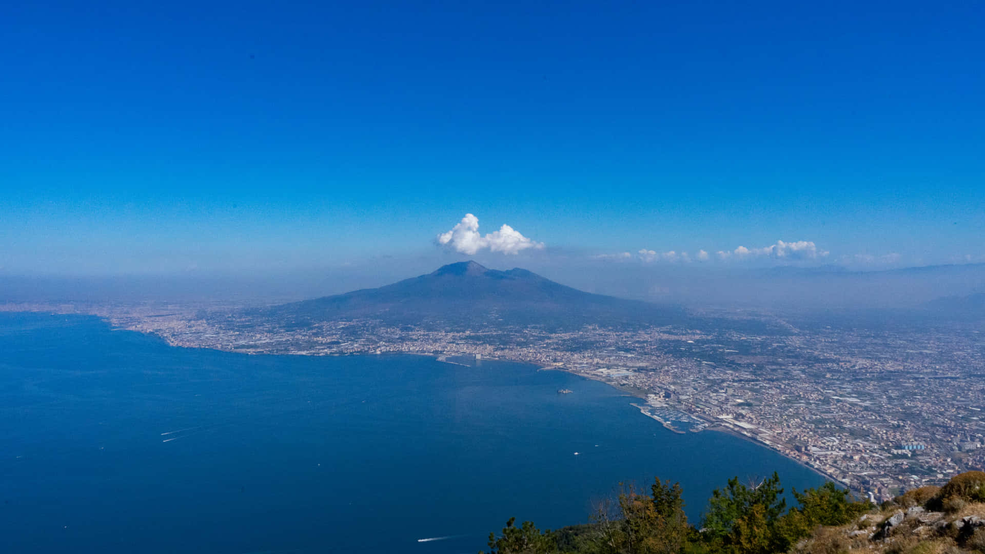 Volcano 桌布 壁紙 — 維蘇威火山的空拍圖，在晴朗藍天下，一股煙霧在拿坡里市和拿坡里灣上空升起。