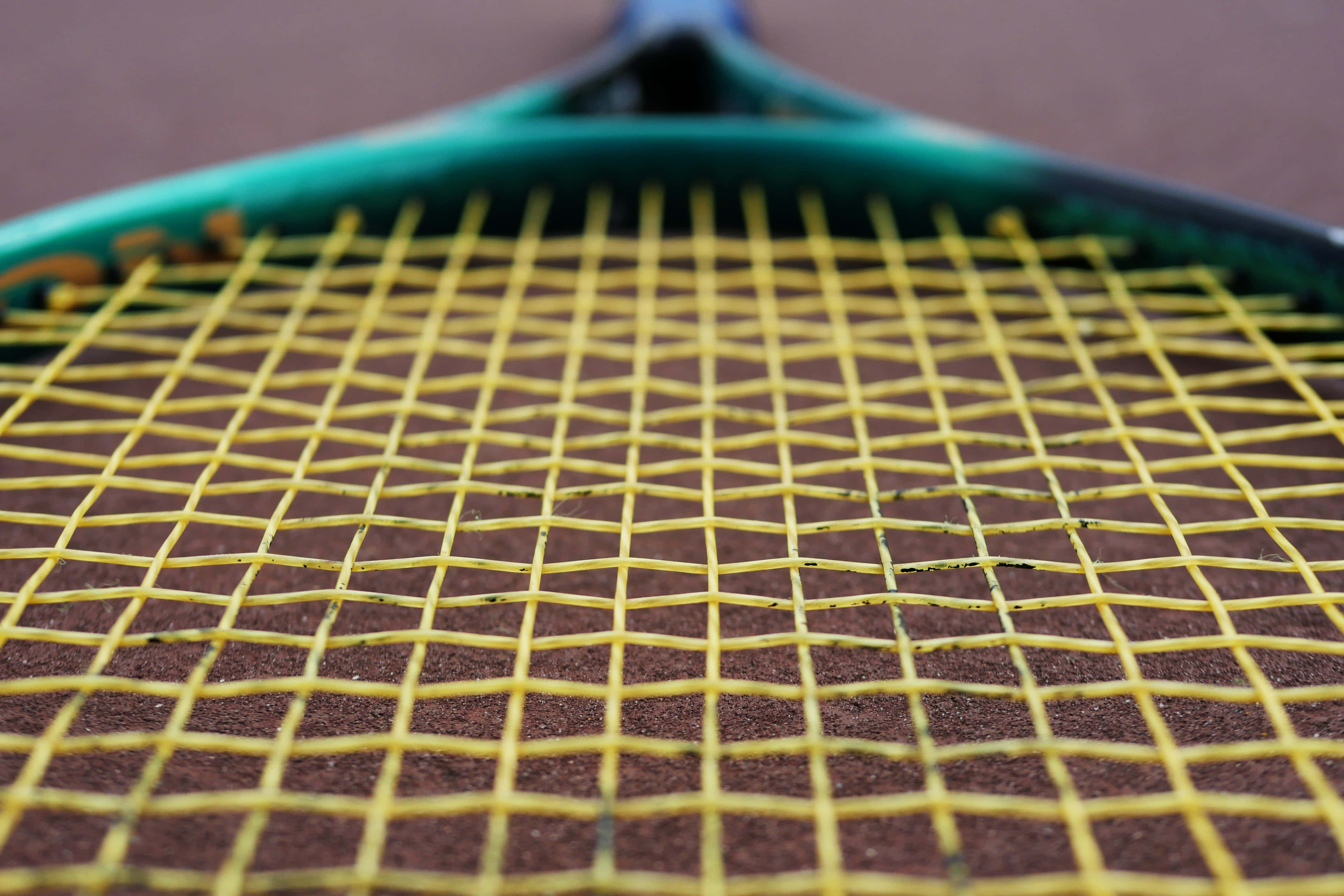 Badminton 桌布 壁紙 — 網球拍黃色線的微距特寫，背景為模糊的紅土球場。