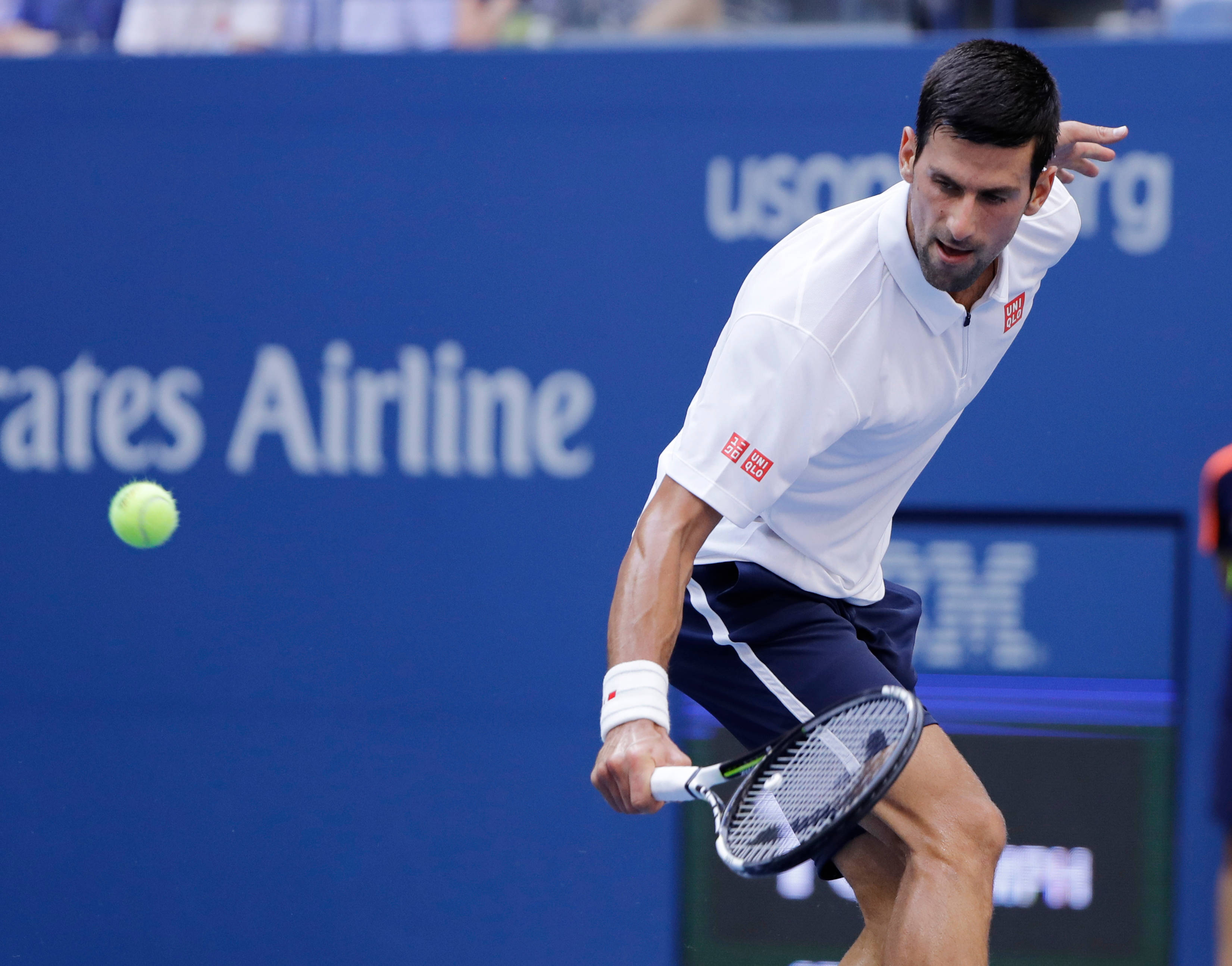 Novak 桌布 壁紙 — 網球運動員諾瓦克·喬科維奇在揮拍中途向前猛衝，擊中一個亮綠色的球，背景是藍色的美國公開賽。