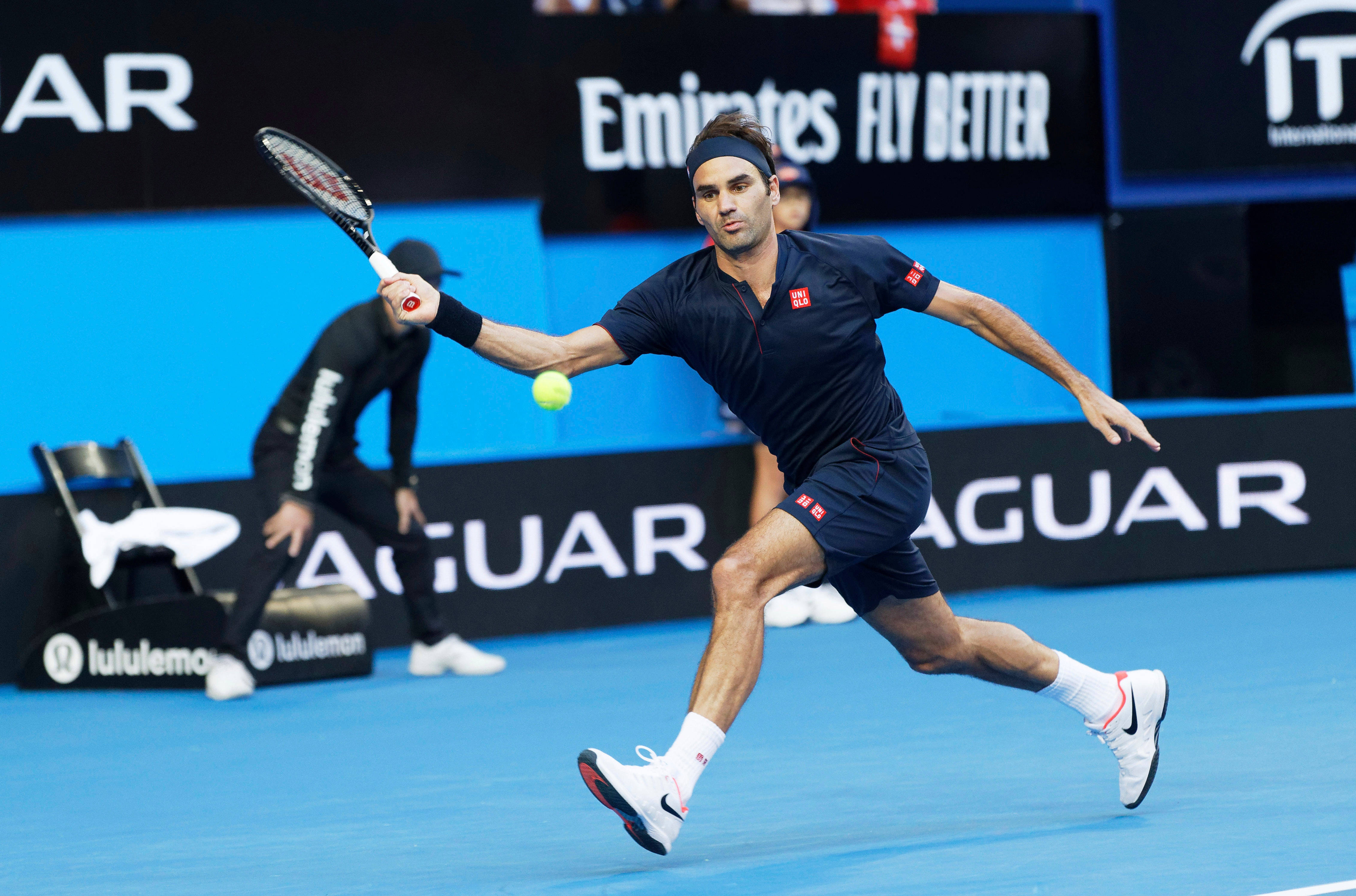 roger 桌布 壁紙 — 網球選手 Roger Federer 在揮拍中途向前猛衝，在明亮的體育場燈光下於充滿活力的藍色球場上擊打黃色球。