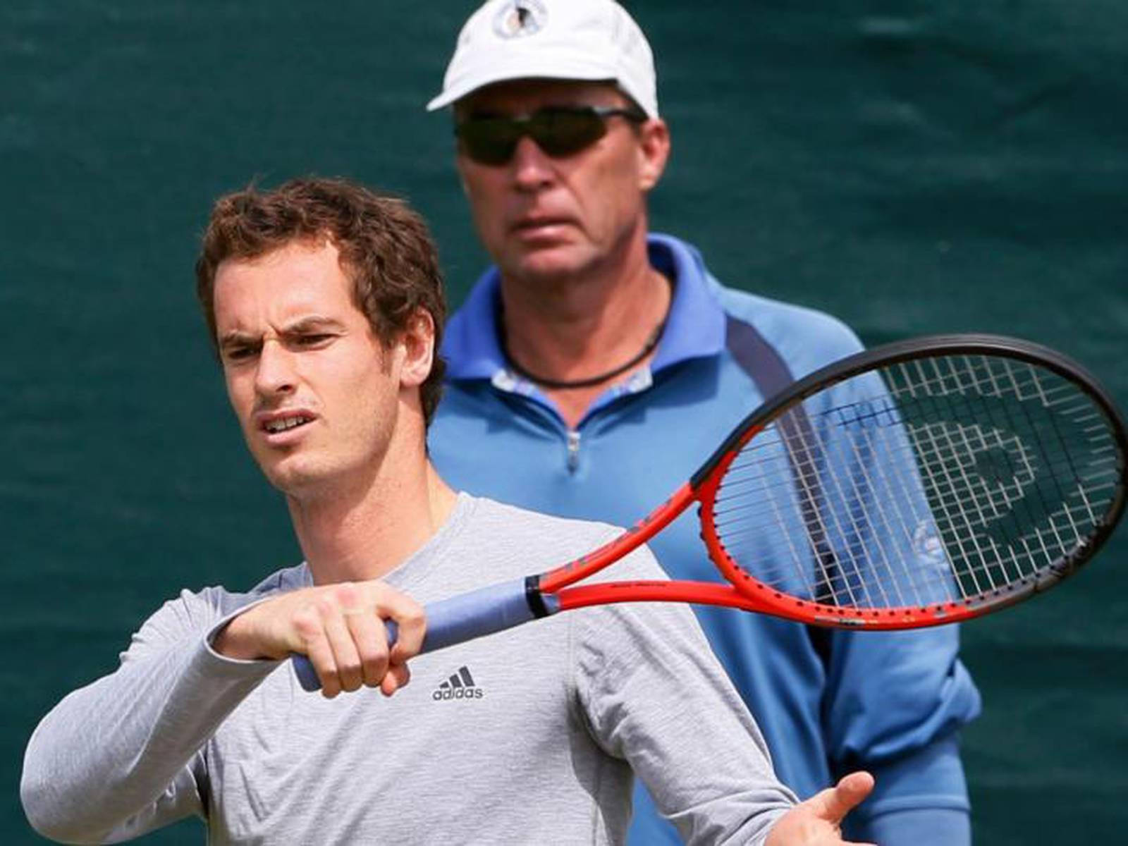 Tennis 桌布 壁紙 — 網球選手在揮拍中握緊球拍，教練在綠色球場背景下專注地觀看。
