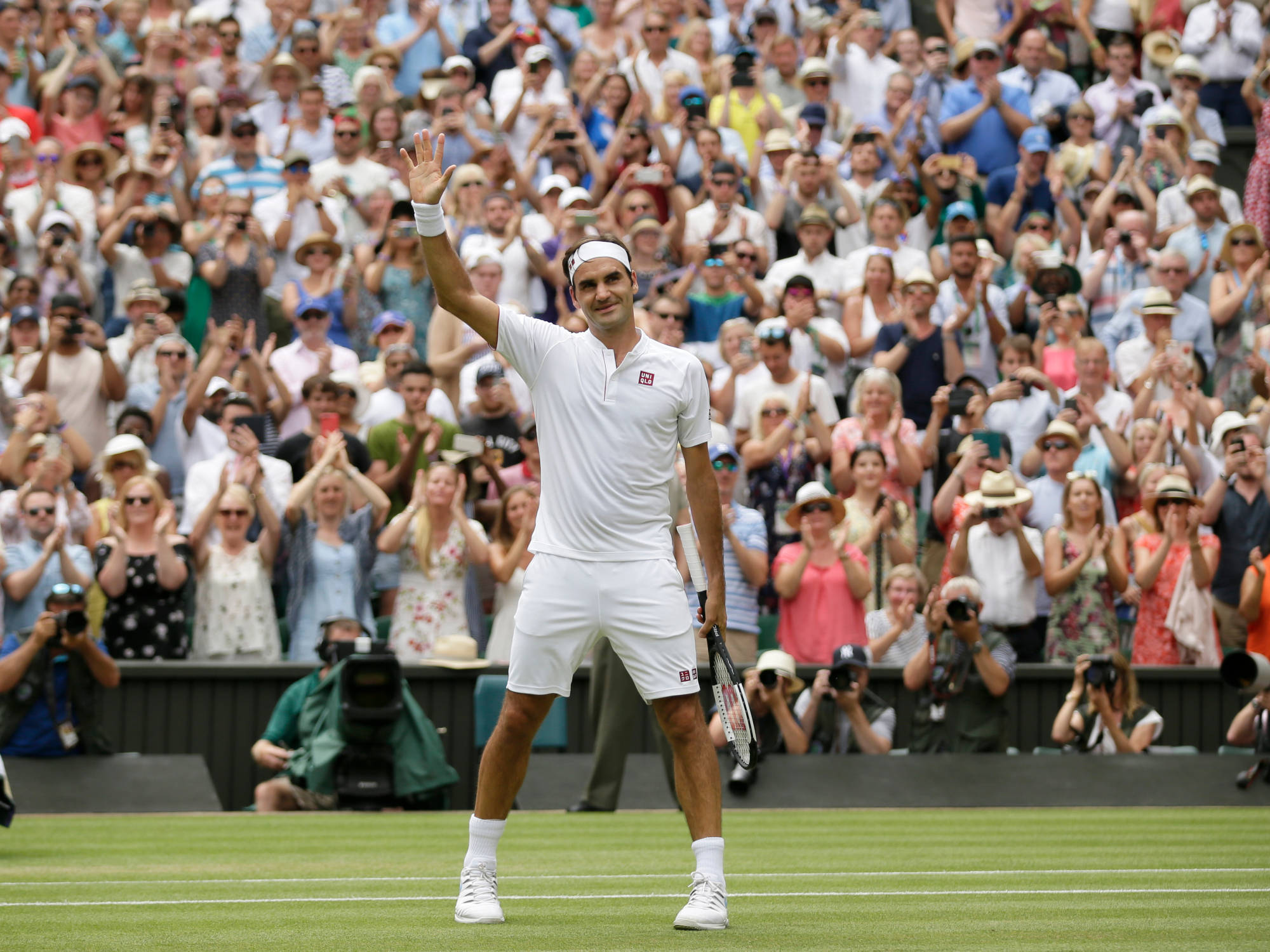 roger 桌布 壁紙 — 網球選手在明亮的日光下向草地場上歡呼的人群揮手。