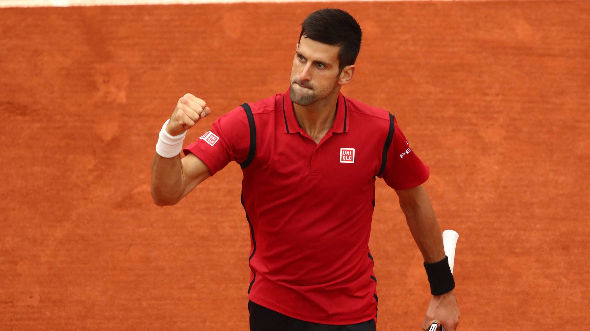 Novak 桌布 壁紙 — 網球選手諾瓦克·喬科維奇在充滿活力的橙色紅土球場上握拳慶祝勝利。