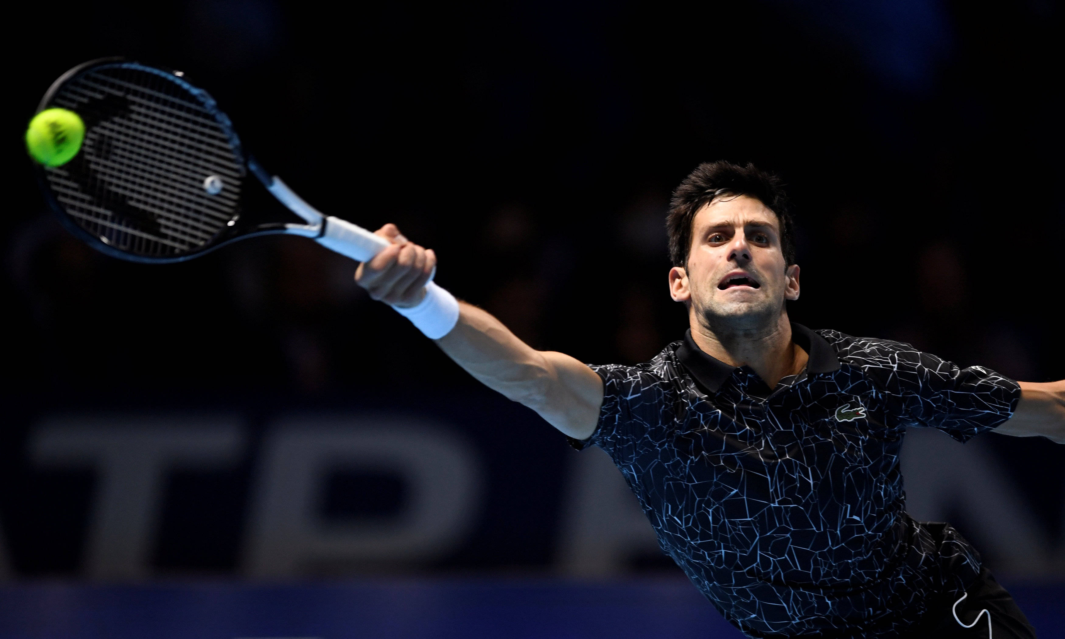 Novak 桌布 壁紙 — 網球選手諾瓦克·喬科維奇在場館燈光下的一場激烈比賽中，揮拍擊向一個亮黃色的網球。