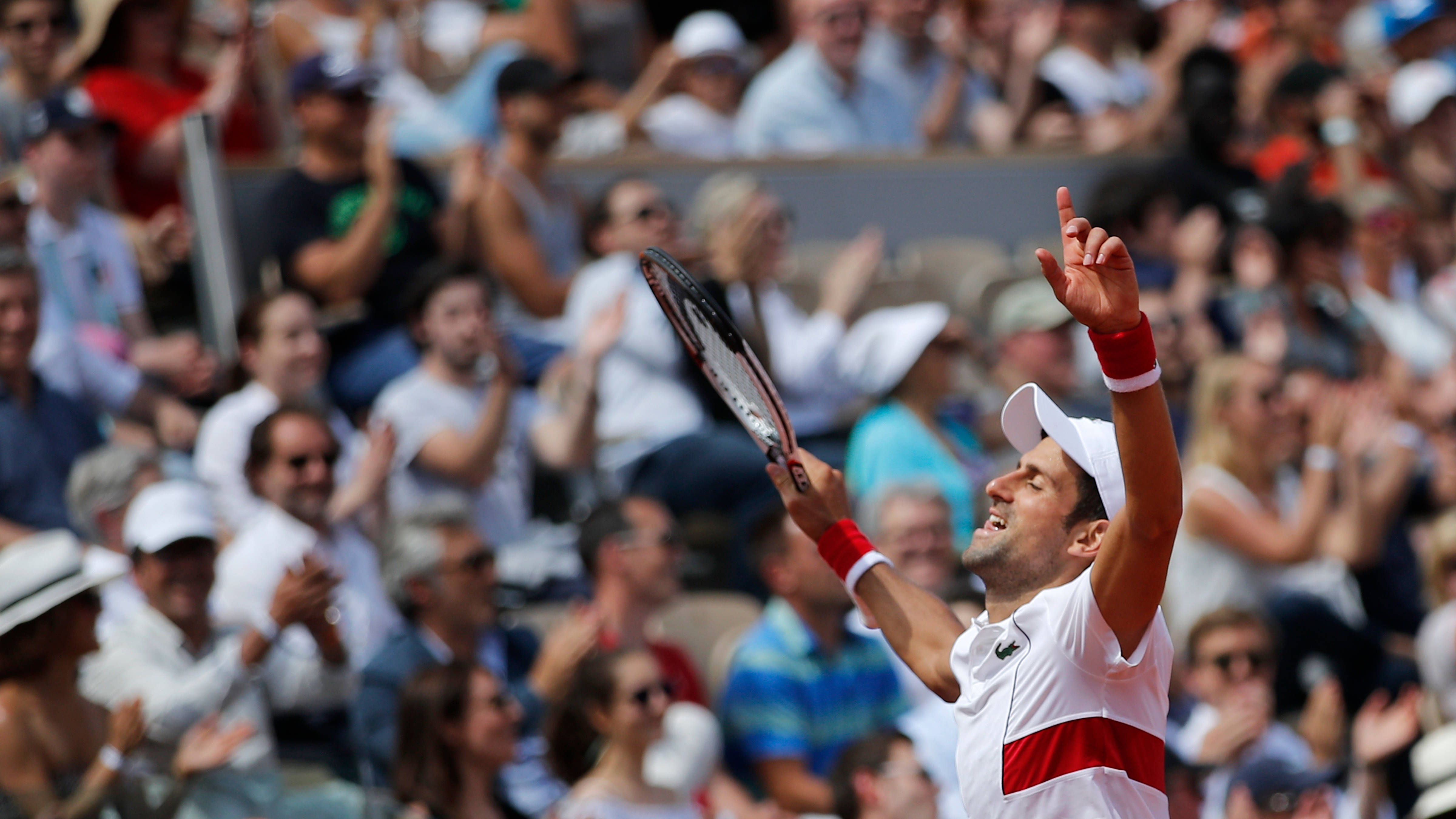Novak 桌布 壁紙 — 網球選手高舉球拍和手指慶祝勝利，歡呼的觀眾在明亮的日光下鼓掌。