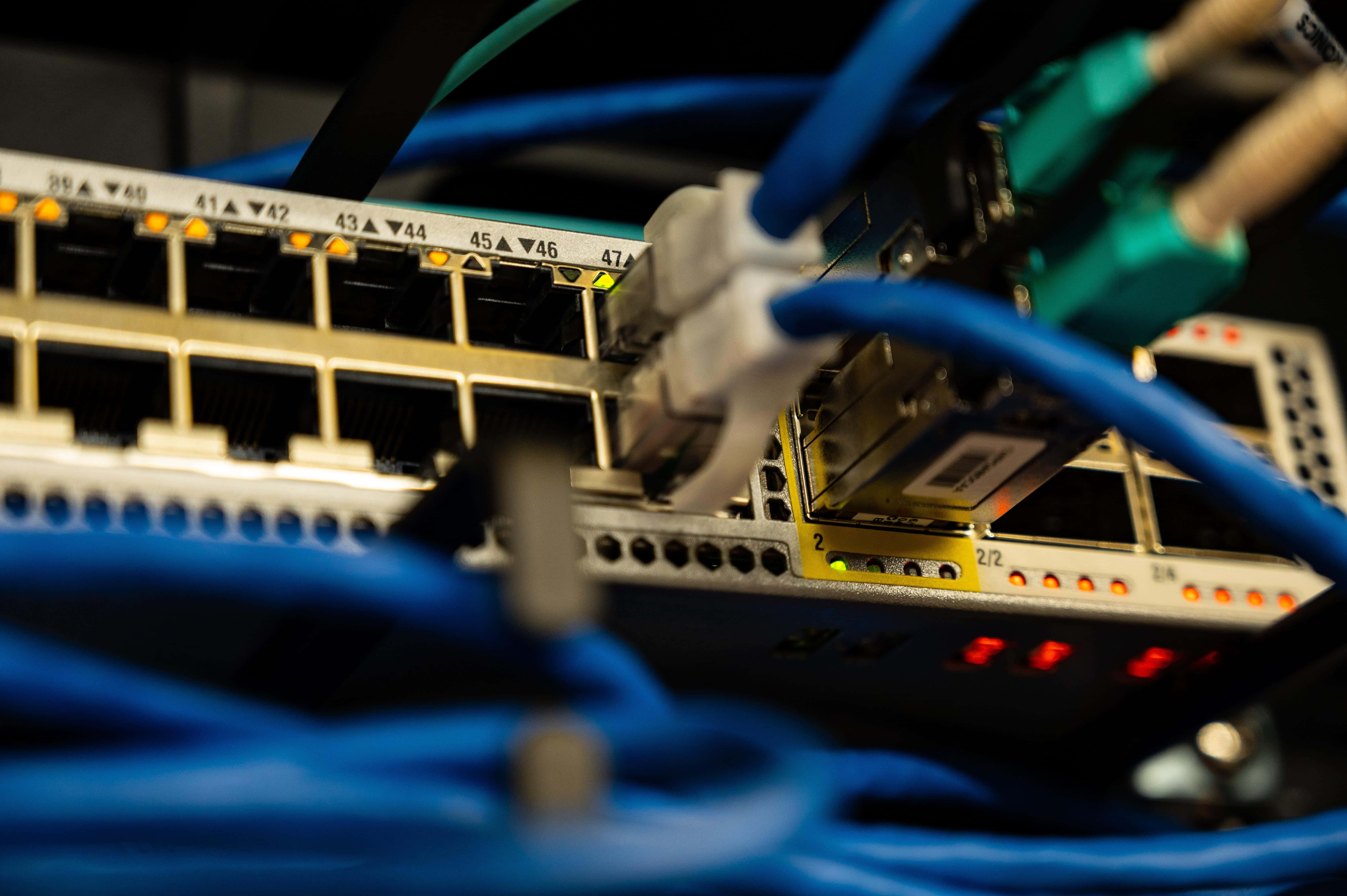 Ethernet 桌布 壁紙 — 網路交換器特寫，插有藍色乙太網路線，指示燈呈琥珀色和紅色發光。