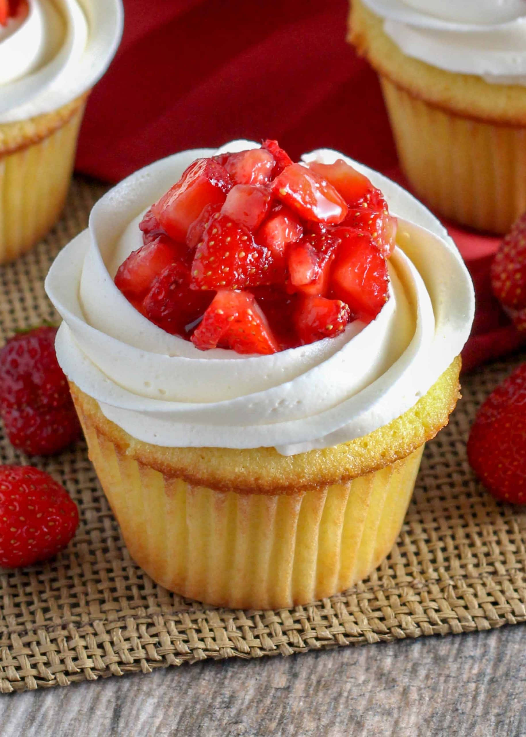 Cupcake 桌布 壁紙 — 編織墊上的草莓紙杯蛋糕，上面有鮮奶油和新鮮切丁草莓的特寫。