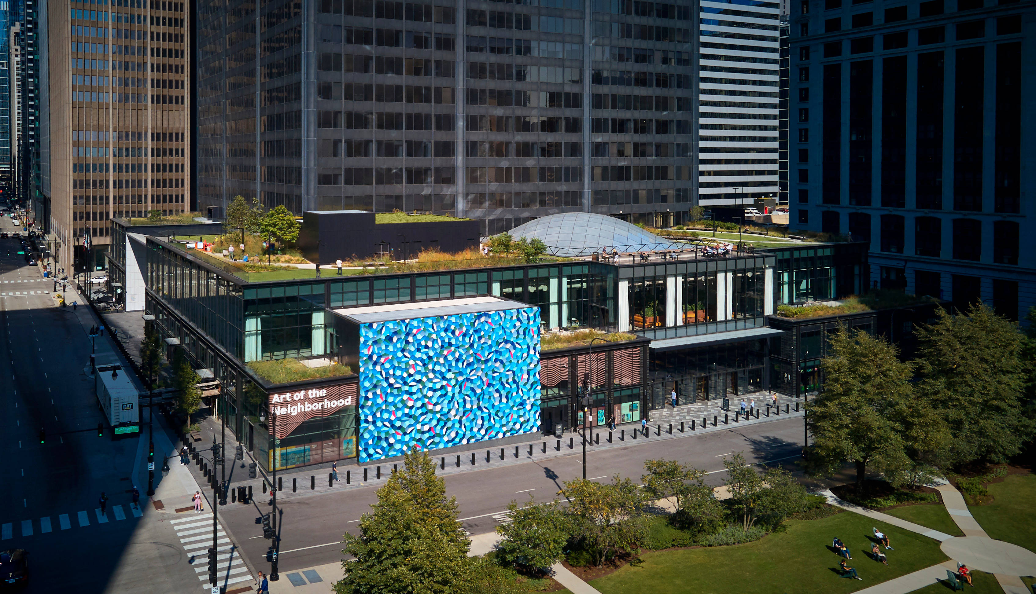 Buildings 桌布 壁紙 — 繁忙城市中一座現代玻璃建築的鳥瞰圖，建築物擁有充滿活力的藍色魚紋外牆和綠色屋頂花園。