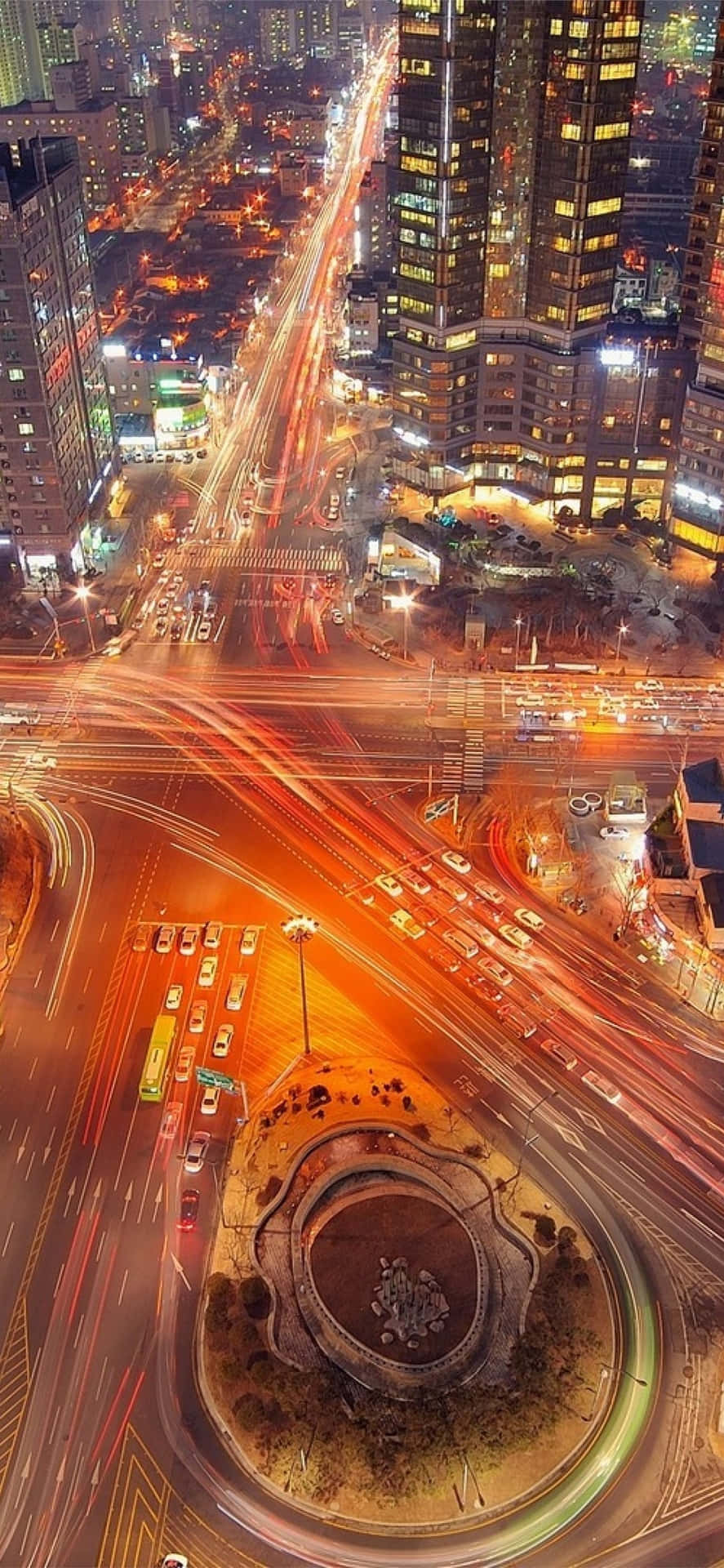 time lapse 桌布 壁紙 — 繁忙城市十字路口的夜間鳥瞰圖，移動車輛的發光軌跡穿梭於高聳的摩天大樓之間。