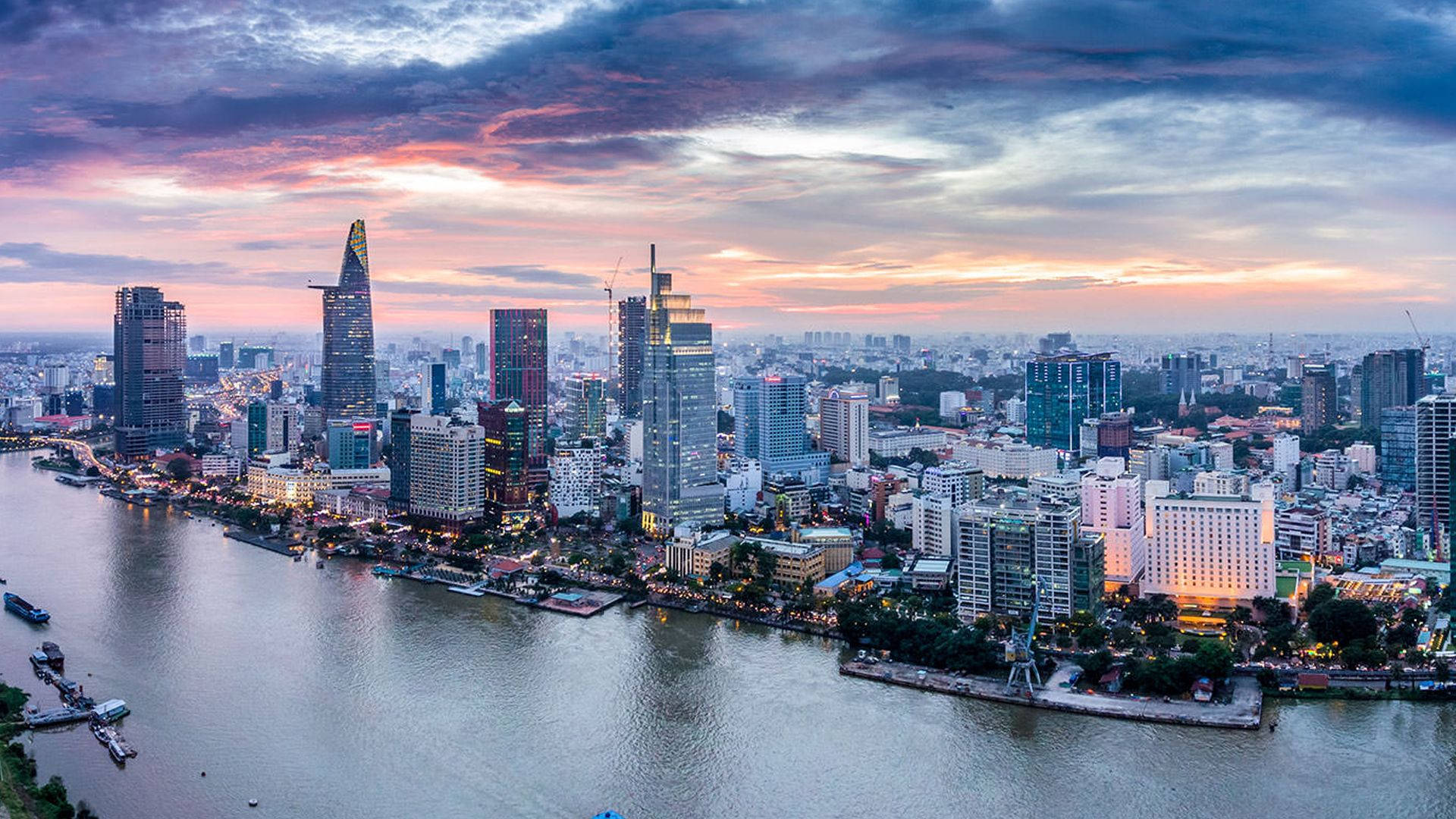 Ho Chi Minh City 桌布 壁紙 — 繁忙城市天際線的鳥瞰圖，日落時分，粉橙色雲彩倒映在寬闊的河流上。