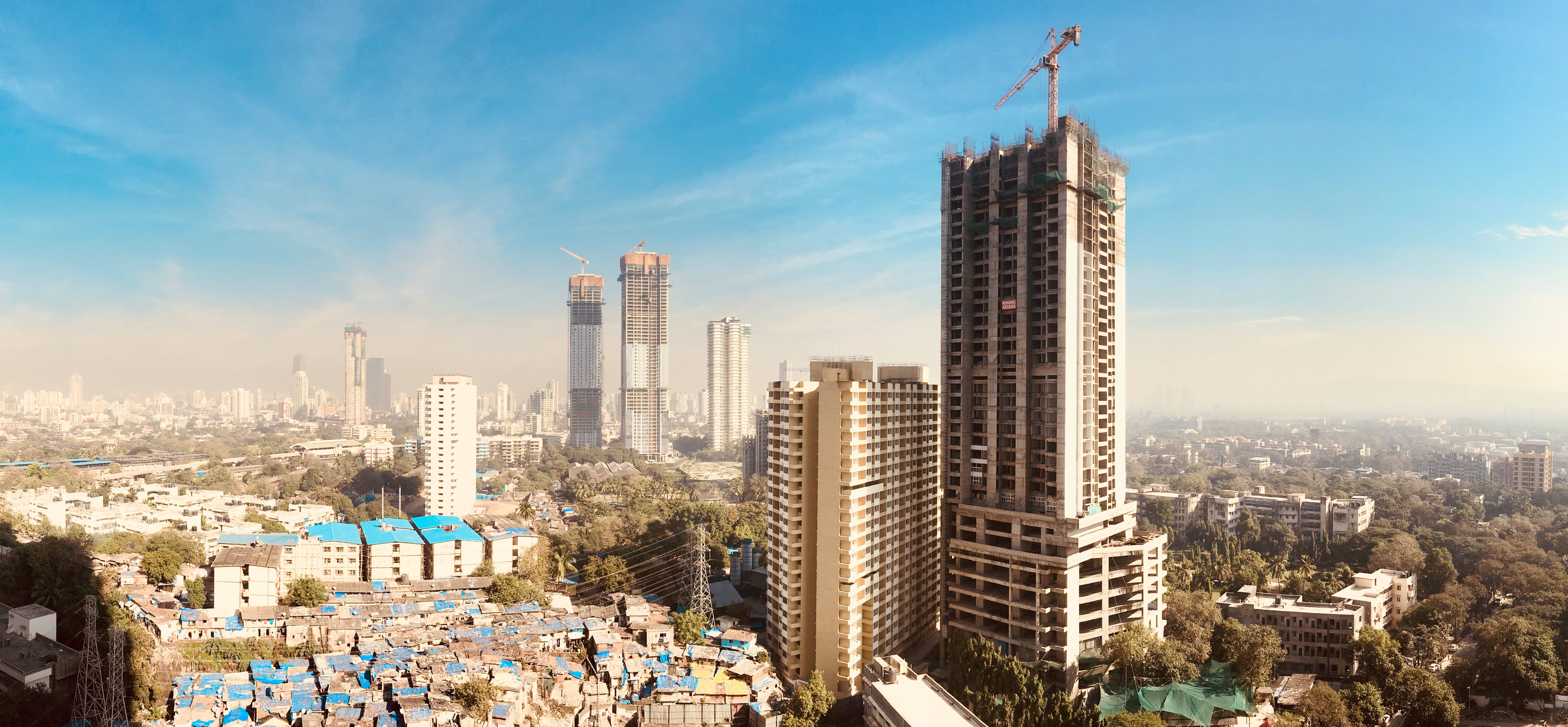 Mumbai 桌布 壁紙 — 繁忙城市景觀的全景視圖，有在建的摩天大樓和藍色屋頂的密集定居點，在晴朗的藍天下。