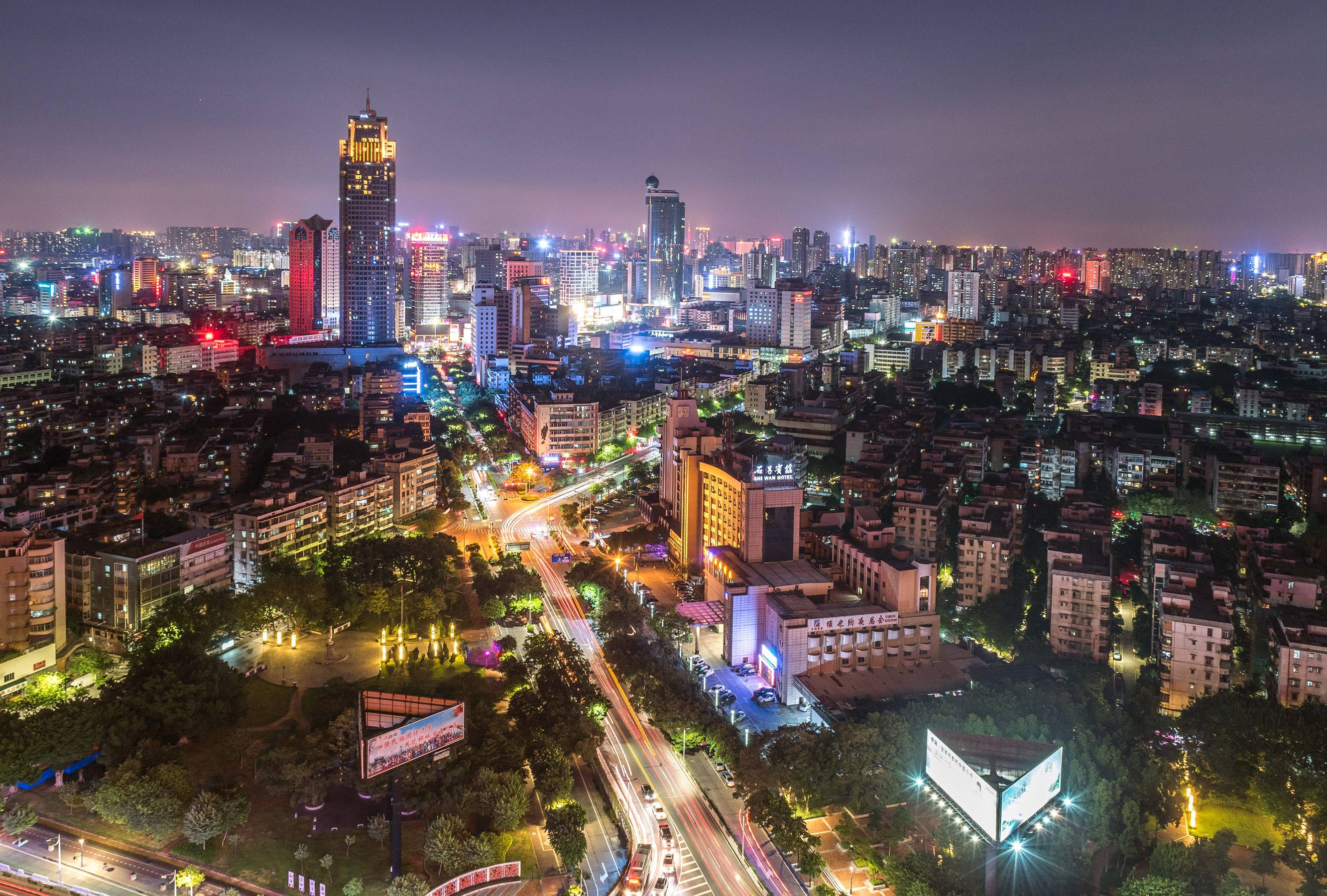 中國 桌布 壁紙 — 繁忙城市景觀的夜間鳥瞰圖，閃爍的摩天大樓和穿梭於密集城市街區的車流光軌。