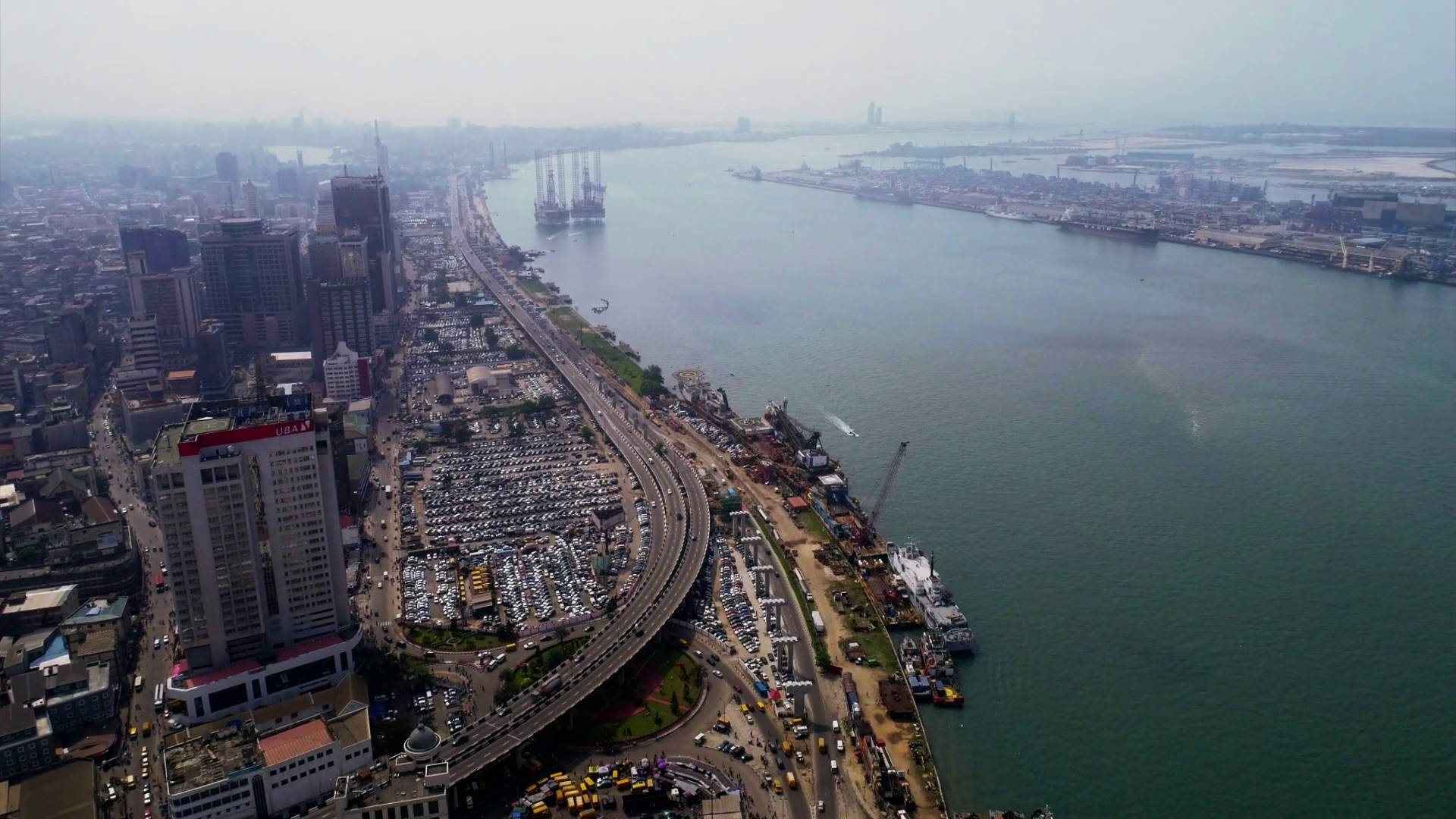 Nigeria 桌布 壁紙 — 繁忙城市景觀的鳥瞰圖，沿著寬闊的河流，有貨船和密集的城市基礎設施，在朦朧的日光下。