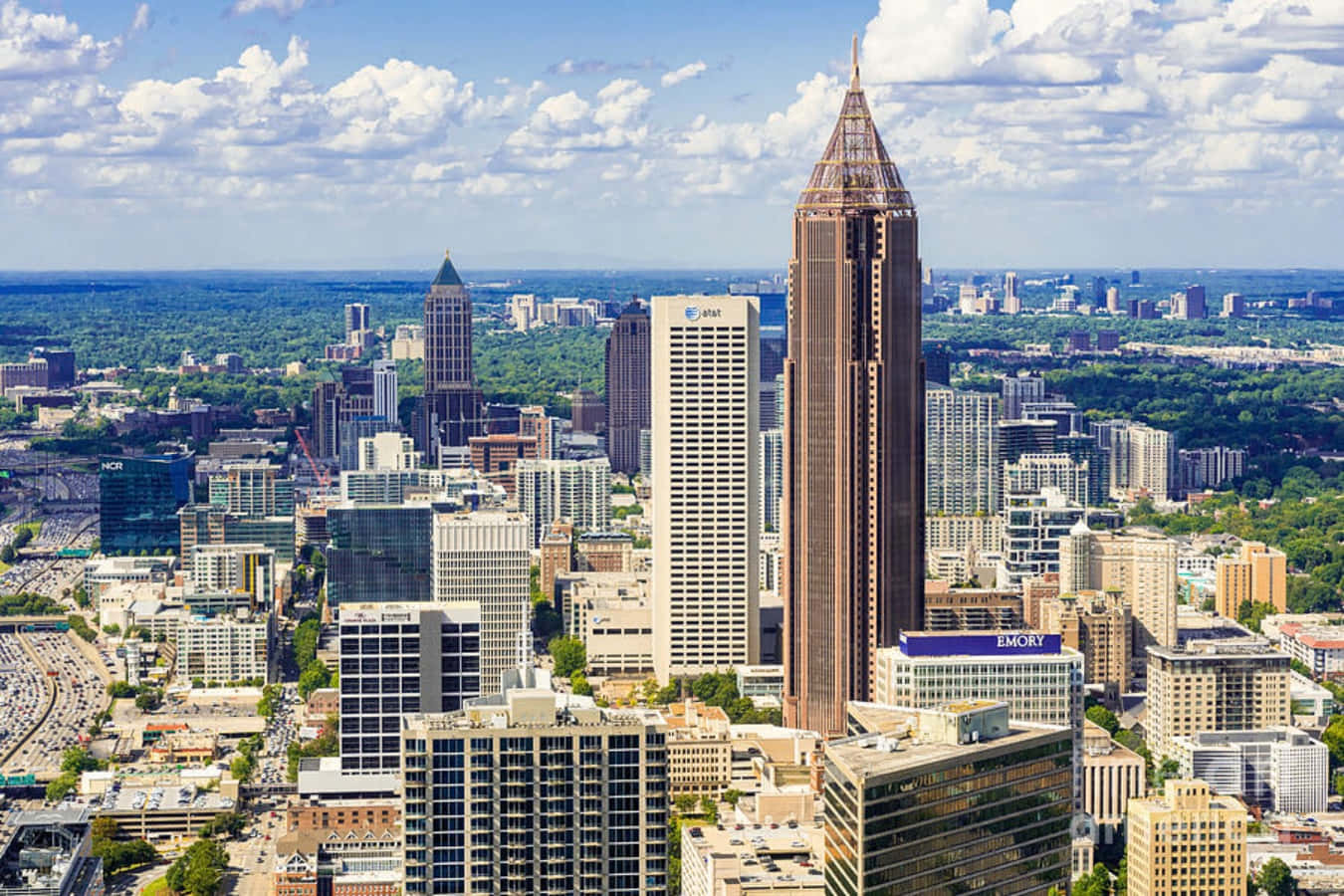 Atlanta Georgia 桌布 壁紙 — 繁忙城市景觀的鳥瞰圖，高聳的摩天大樓和鬱鬱蔥蔥的公園，在明亮的藍天下飄著蓬鬆的白雲。