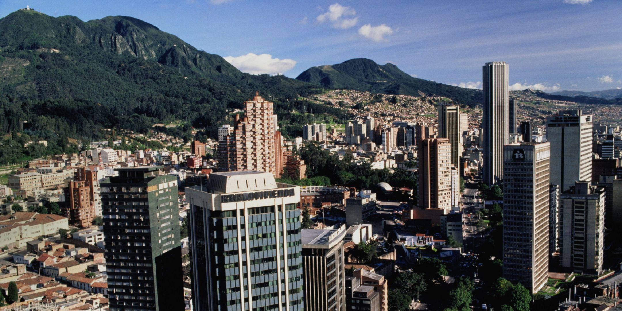 Bogota 桌布 壁紙 — 繁忙城市的空拍圖，坐落於翠綠山巒之間，藍天白雲點綴。