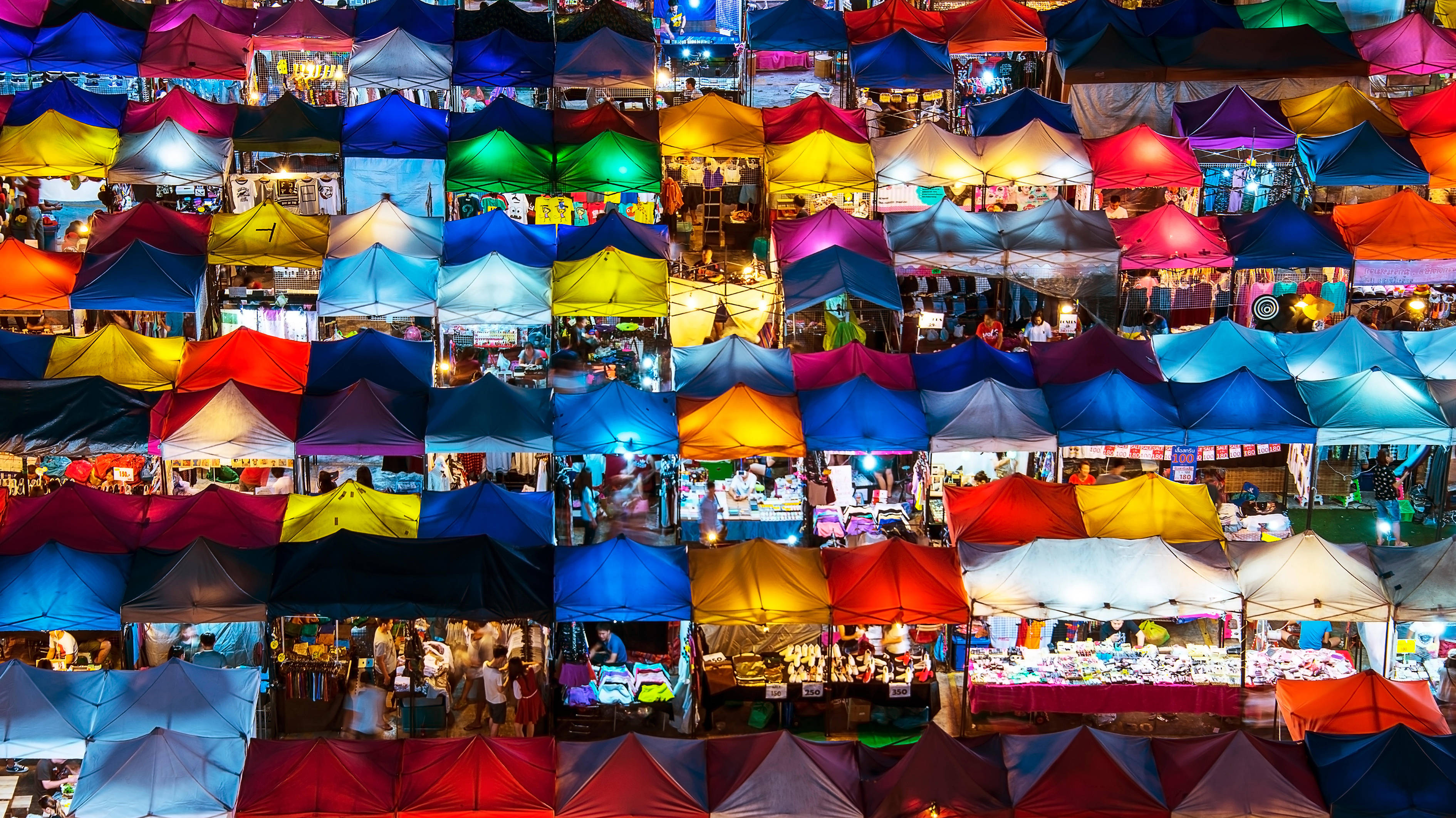 Bangkok 桌布 壁紙 — 繁忙夜市的空拍圖，數以千計色彩繽紛的攤位帳篷在人造燈光下發光。