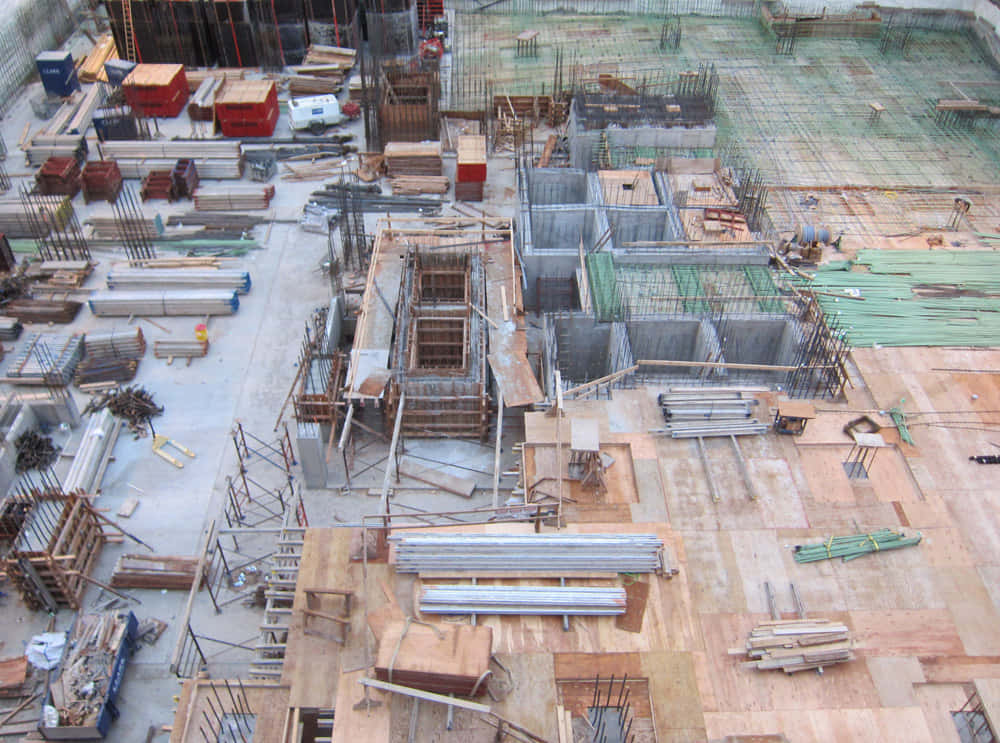 Constructivism 桌布 壁紙 — 繁忙建築工地的鳥瞰圖，有鋼筋、混凝土模板、鷹架和成堆的木材，在明亮的日光下。