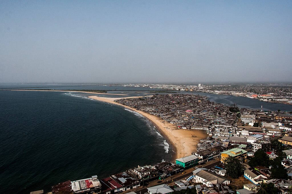 Liberia 桌布 壁紙 — 繁忙海岸城市的鳥瞰圖，沿著彎曲進入深藍色海洋的沙灘上有密集的房屋。