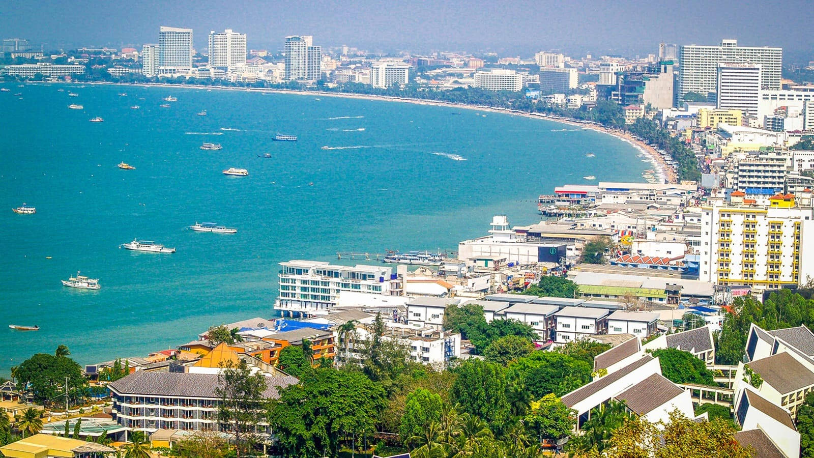 城市 桌布 壁紙 — 繁忙海岸城市的鳥瞰圖，碧綠海水點綴著船隻，密集的城市天際線在晴朗天空下展現。