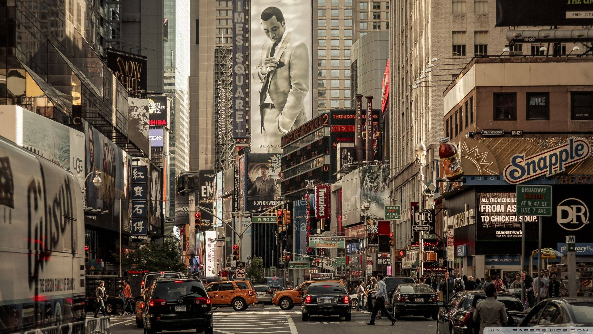 New York 桌布 壁紙 — 繁忙的紐約市街道，充滿高聳的建築物、霓虹燈招牌和行人，在明亮的白天天空下。