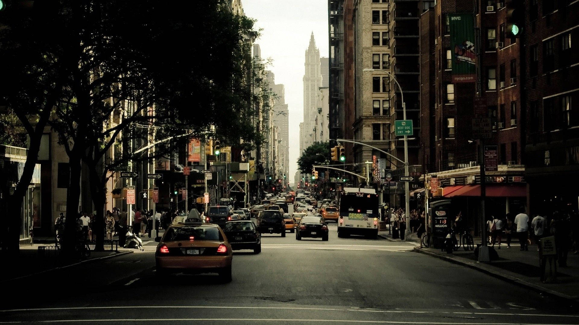Street 桌布 壁紙 — 繁忙的紐約市街道，兩旁高樓大廈林立，人行道旁樹木成蔭，黃色計程車在車流中穿梭。