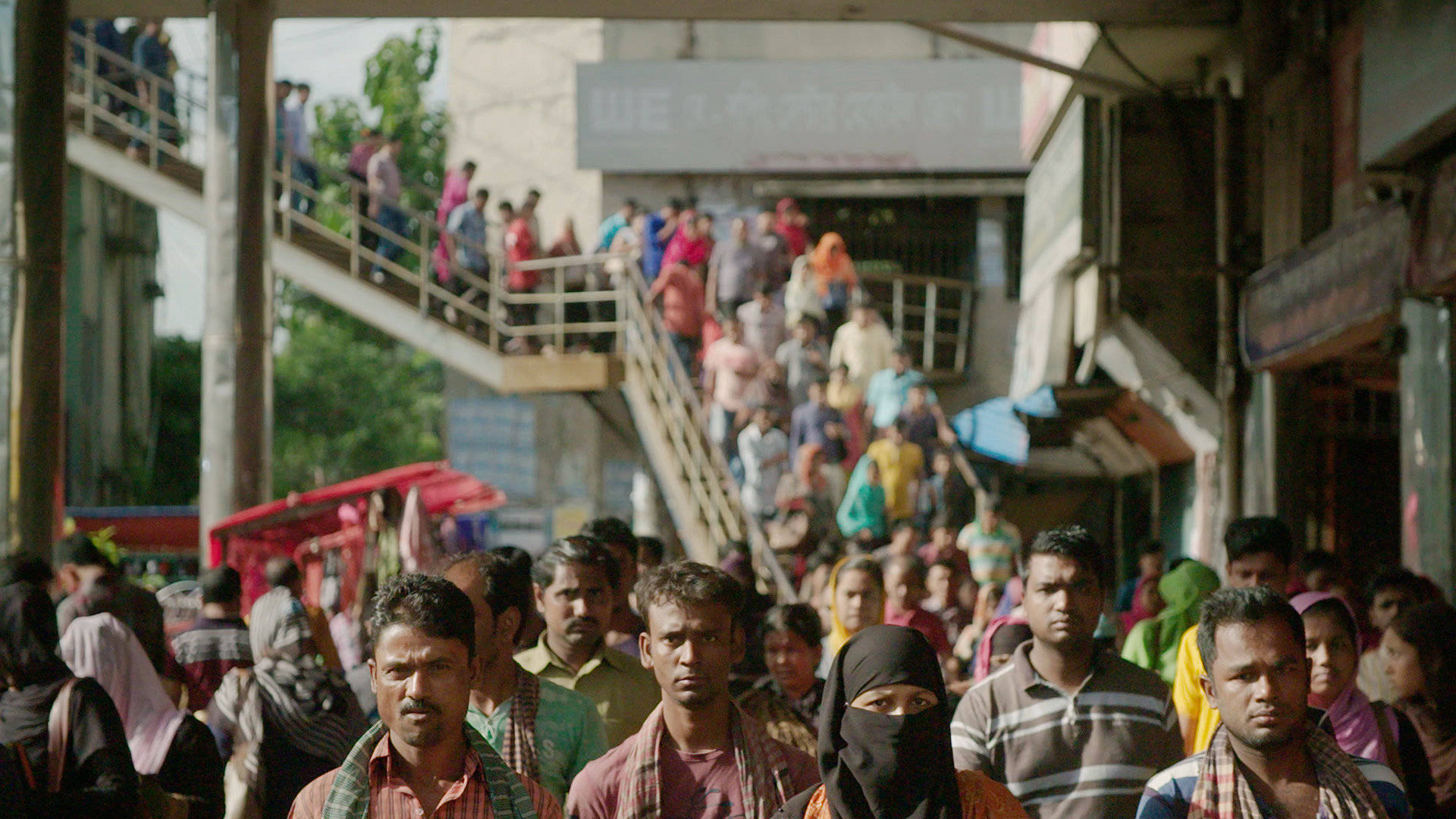 Bangladesh 桌布 壁紙 — 繁忙的都市街景，人群在有蓋人行道和樓梯下行走，周圍是商店和車輛。