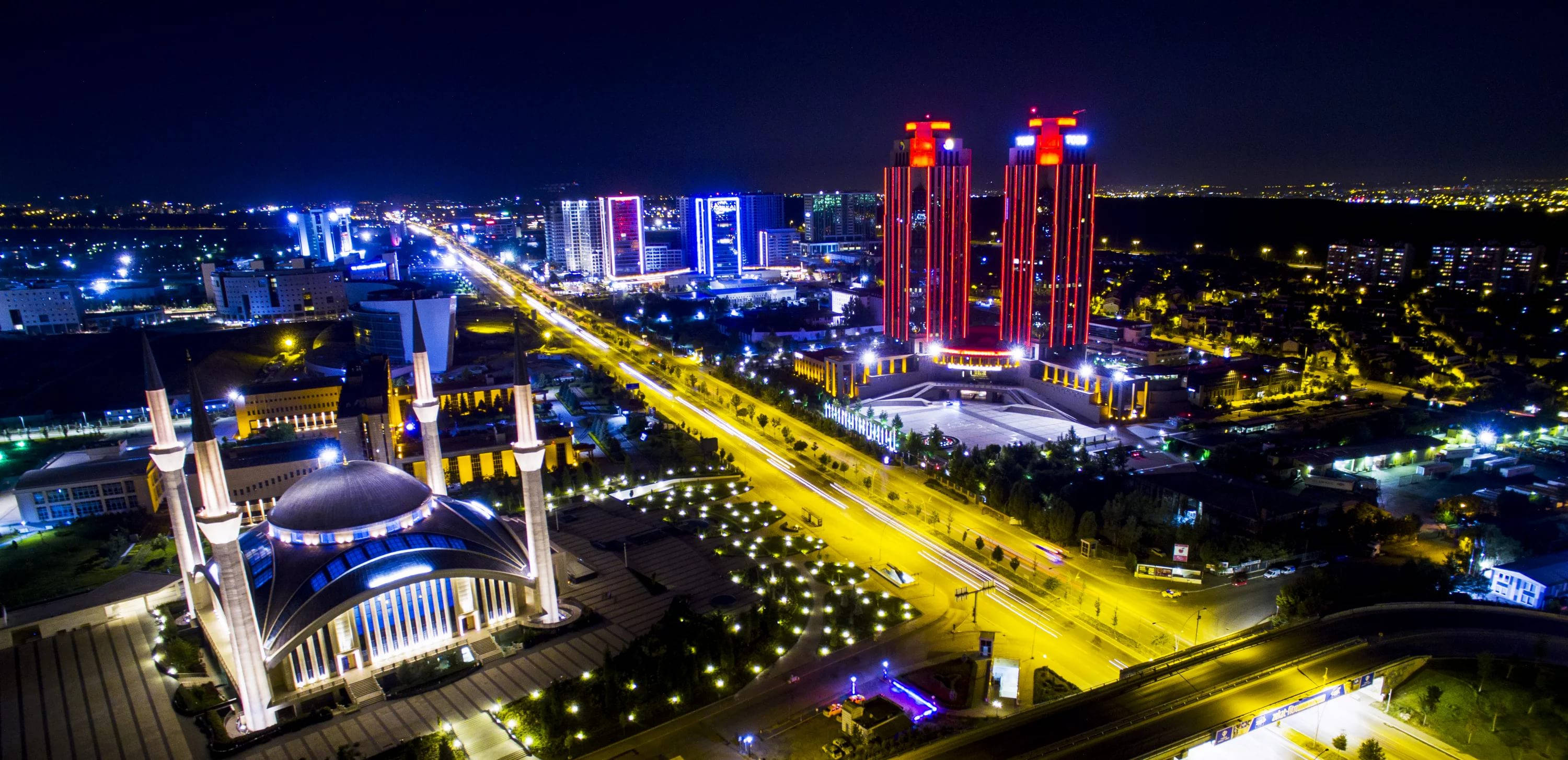 Ankara 桌布 壁紙 — 繁忙高速公路旁，一座發光的清真寺和燈火通明的摩天大樓構成的充滿活力的城市景觀的夜間空拍圖。