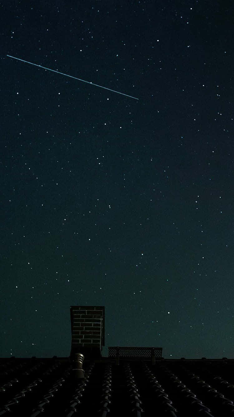 Dark Sky 桌布 壁紙 — 繁星點點的夜空，一顆明亮的流星劃過黑暗的瓦片屋頂和磚砌煙囪上方。