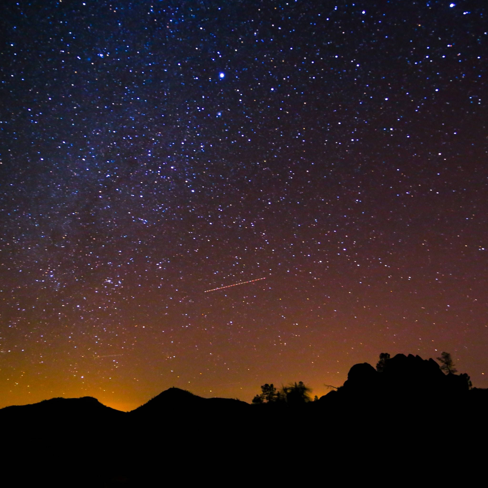 Sky HD 桌布 壁紙 — 繁星點點的夜空，一顆明亮的流星劃過黑暗的山脈輪廓，映襯著橙色的地平線。
