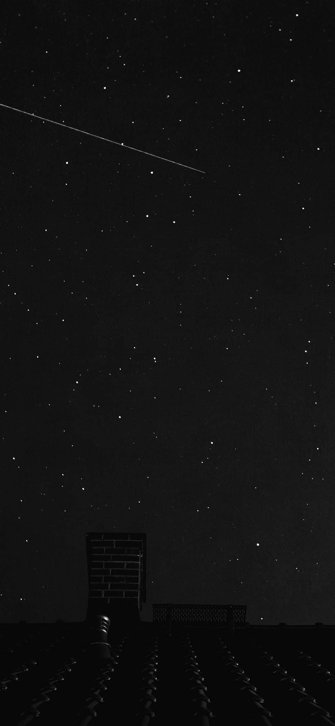 iPhone 11 Pro Black 桌布 壁紙 — 繁星點點的夜空，一顆明亮的流星劃過黑暗的屋頂煙囪上方。