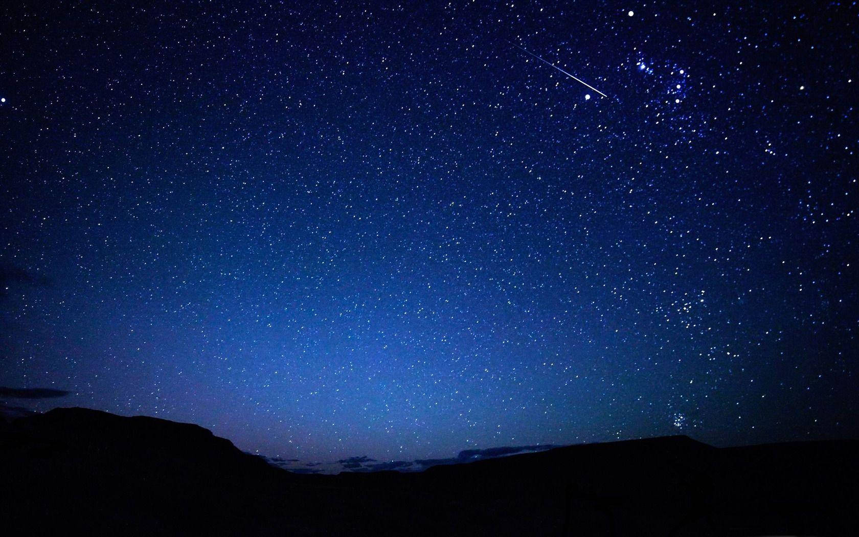 夜空 桌布 壁紙 — 繁星點點的夜空，一顆明亮的流星劃過黑暗的山巒輪廓之上。