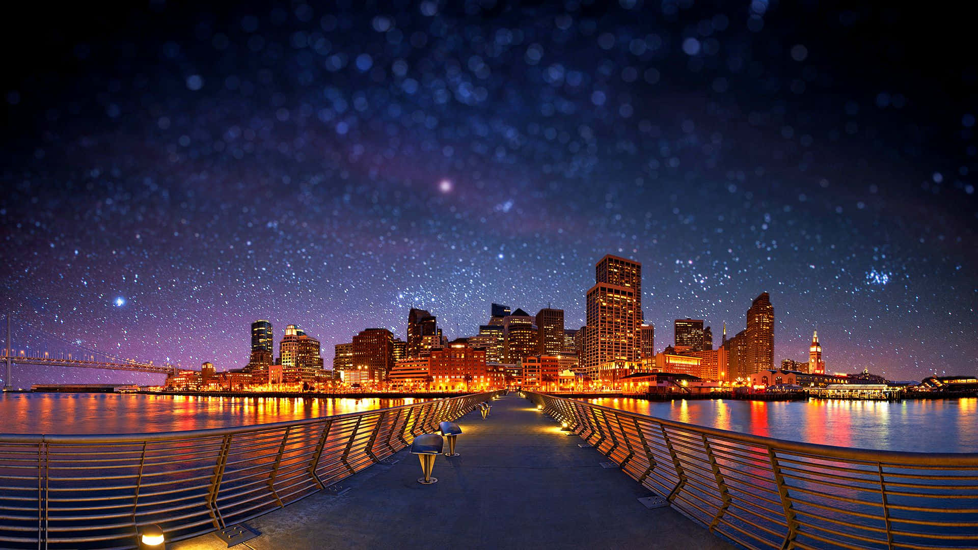Pier 桌布 壁紙 — 繁星點點的夜空，下方是發光的城市天際線，倒映在平靜的水面上，一條燈火通明的小徑通向它。