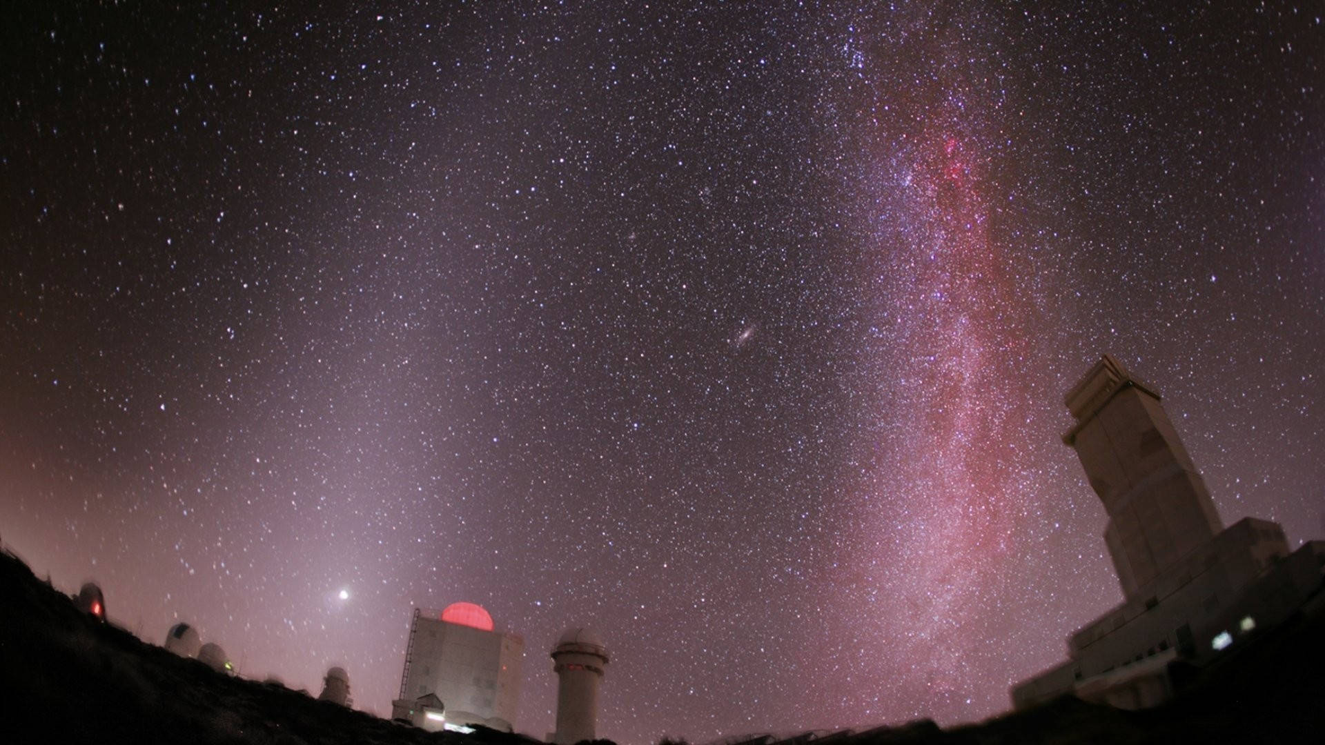 1920x1080 高畫質自然 桌布 壁紙 — 繁星點點的夜空，充滿活力的粉紫色銀河在黑暗山坡上的天文台圓頂上方拱起。