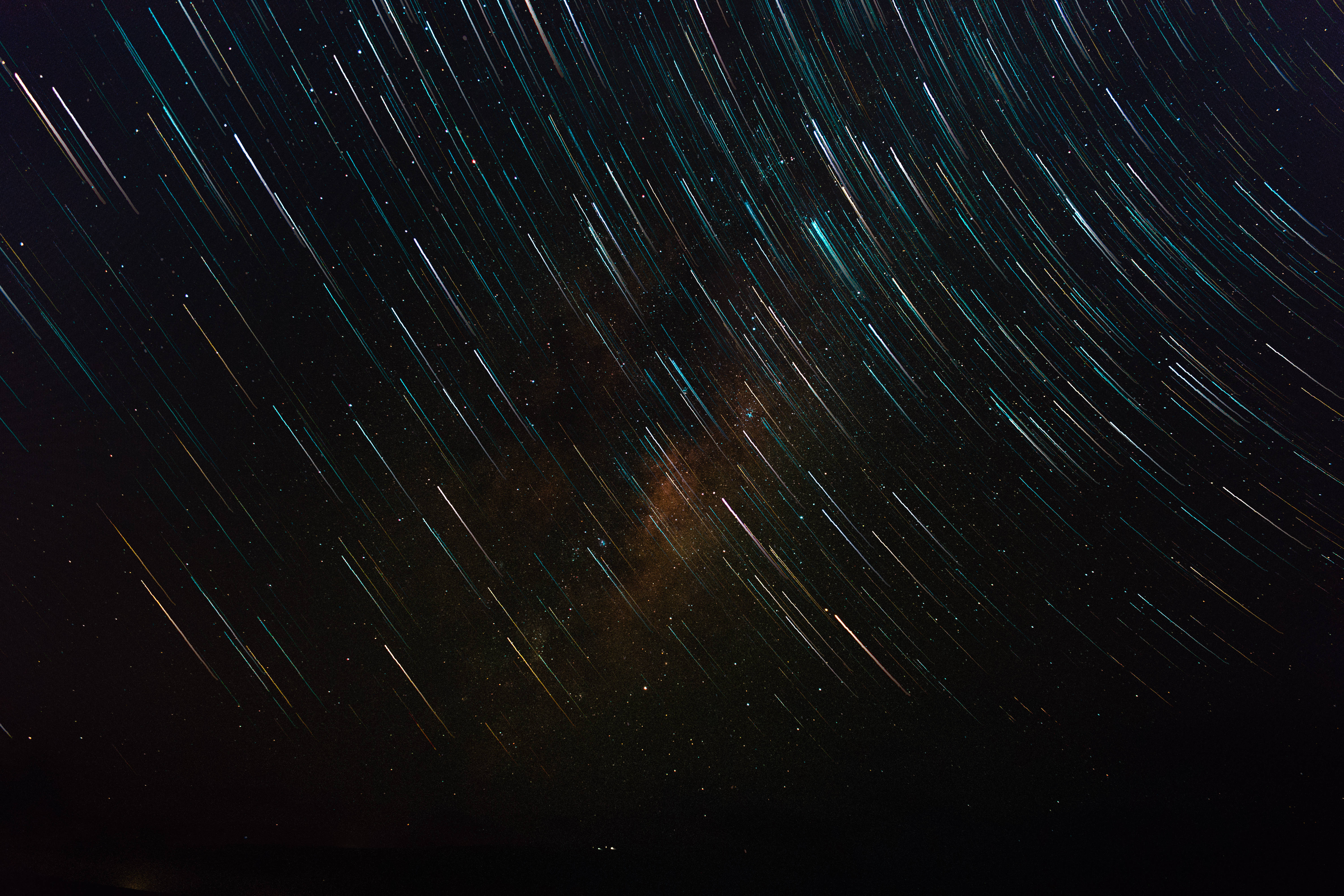 外星人 桌布 壁紙 — 繁星點點的夜空，充滿活力的藍綠色和金色星軌圍繞著發光的星雲核心旋轉。