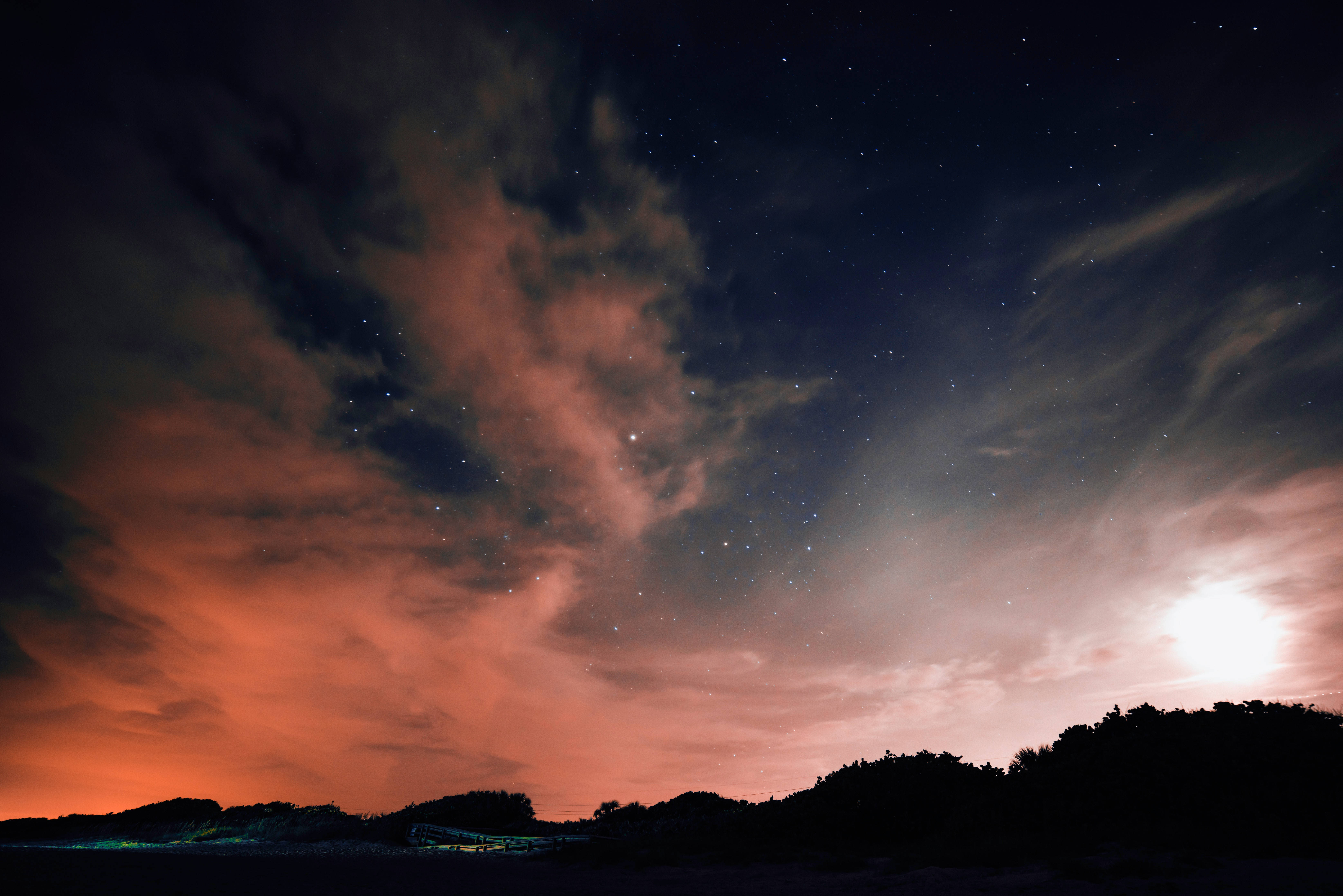 夜空 桌布 壁紙 — 繁星點點的夜空，有火紅色的橙雲和明亮的月亮，映襯著黑暗的山丘剪影。