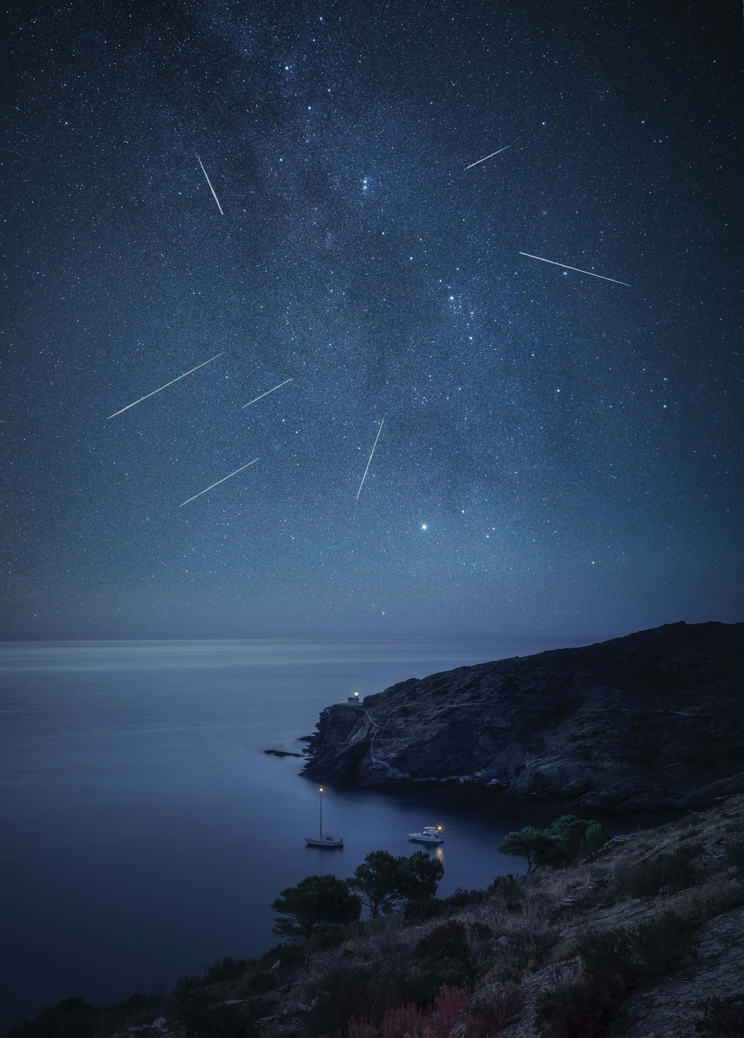 meteor 桌布 壁紙 — 繁星點點的夜空，流星弧線劃過平靜的海面和岩石海岸，點亮的船隻點綴其間。