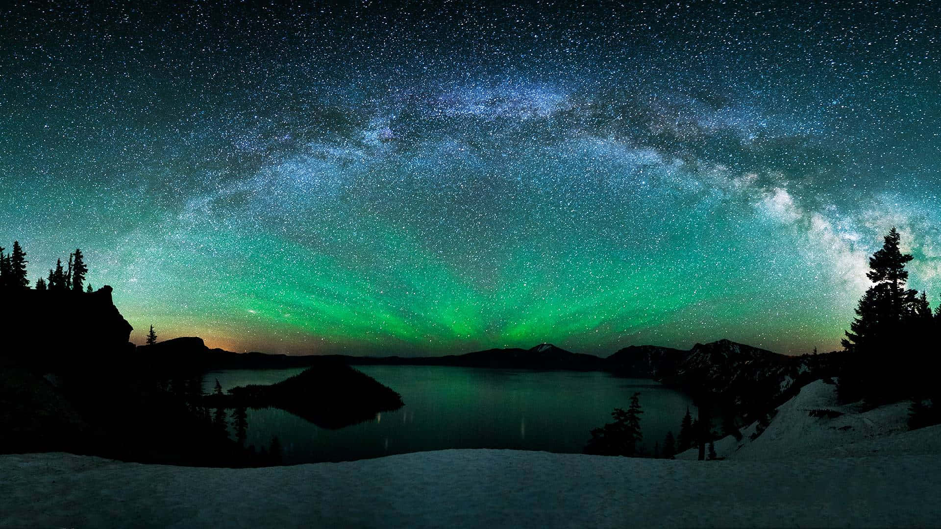極光 桌布 壁紙 — 繁星點點的夜空，銀河和綠色北極光映照在白雪覆蓋的湖面上，四周環繞著深色樹木。