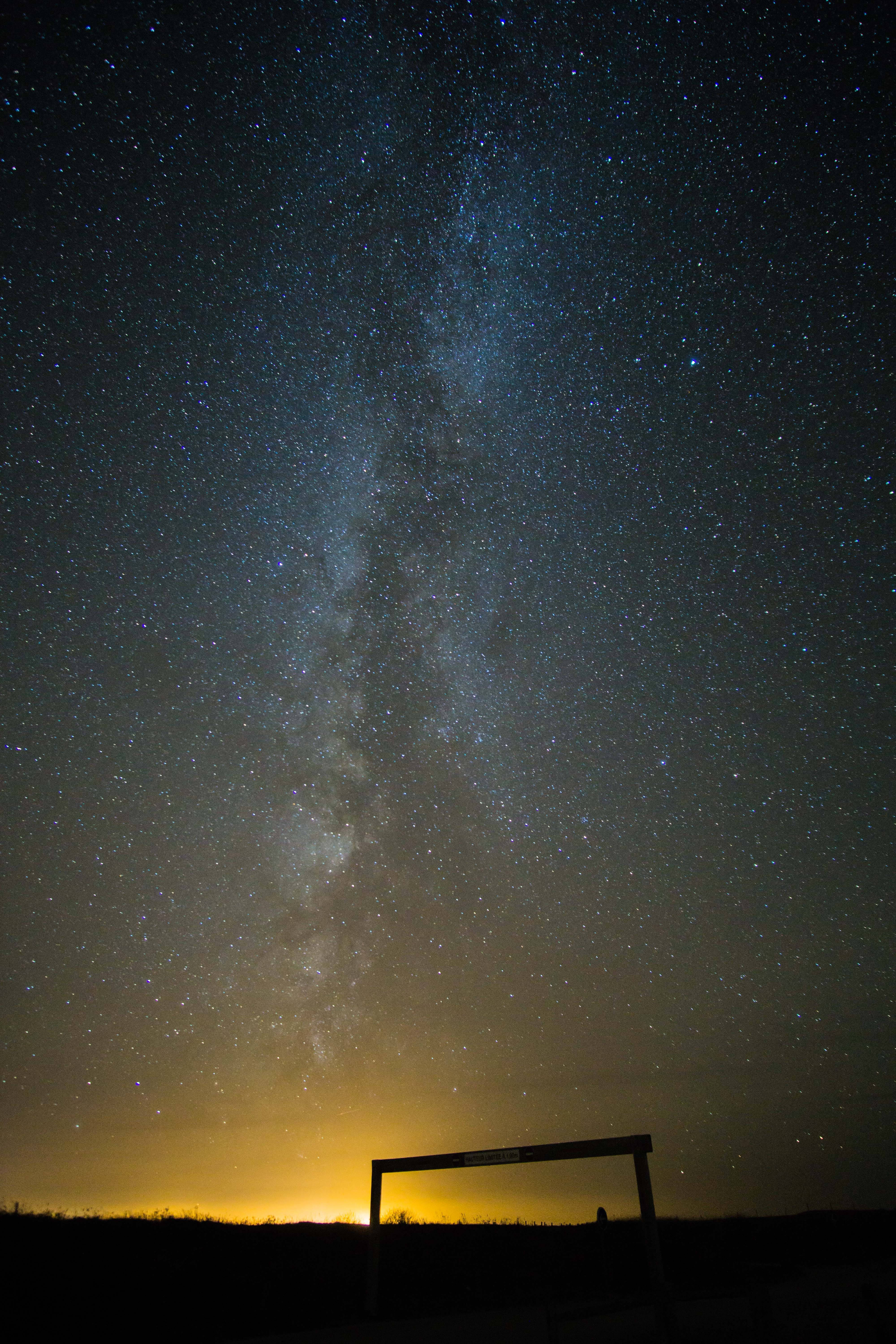 Milky 桌布 壁紙 — 繁星點點的夜空，銀河在剪影大門上方拱起，映襯著發光的地平線。