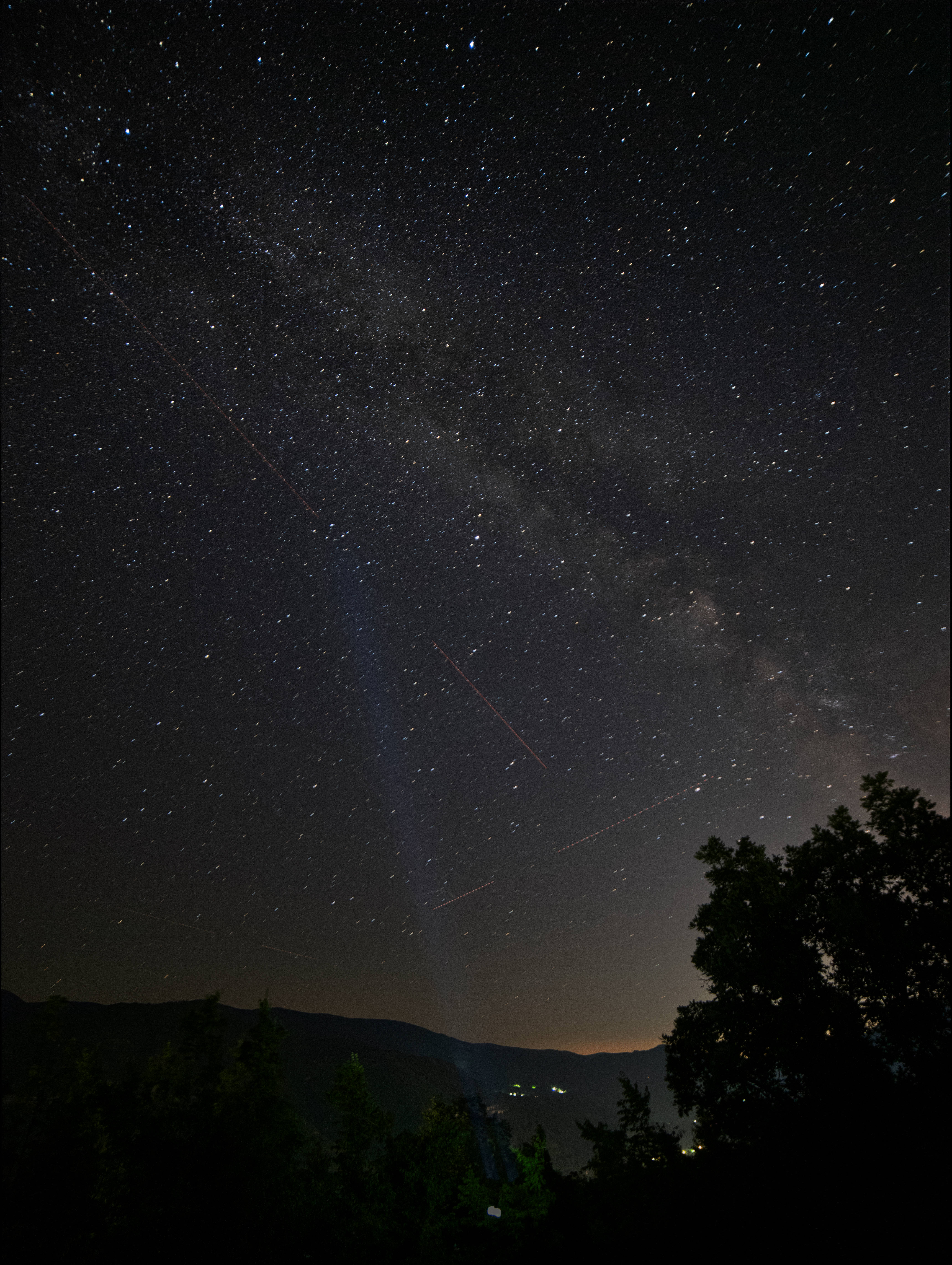 iOS 16 壁紙 桌布 壁紙 — 繁星點點的夜空，銀河在剪影般的樹木和遠山之上拱起，籠罩在黑暗天鵝絨般的廣闊空間中。