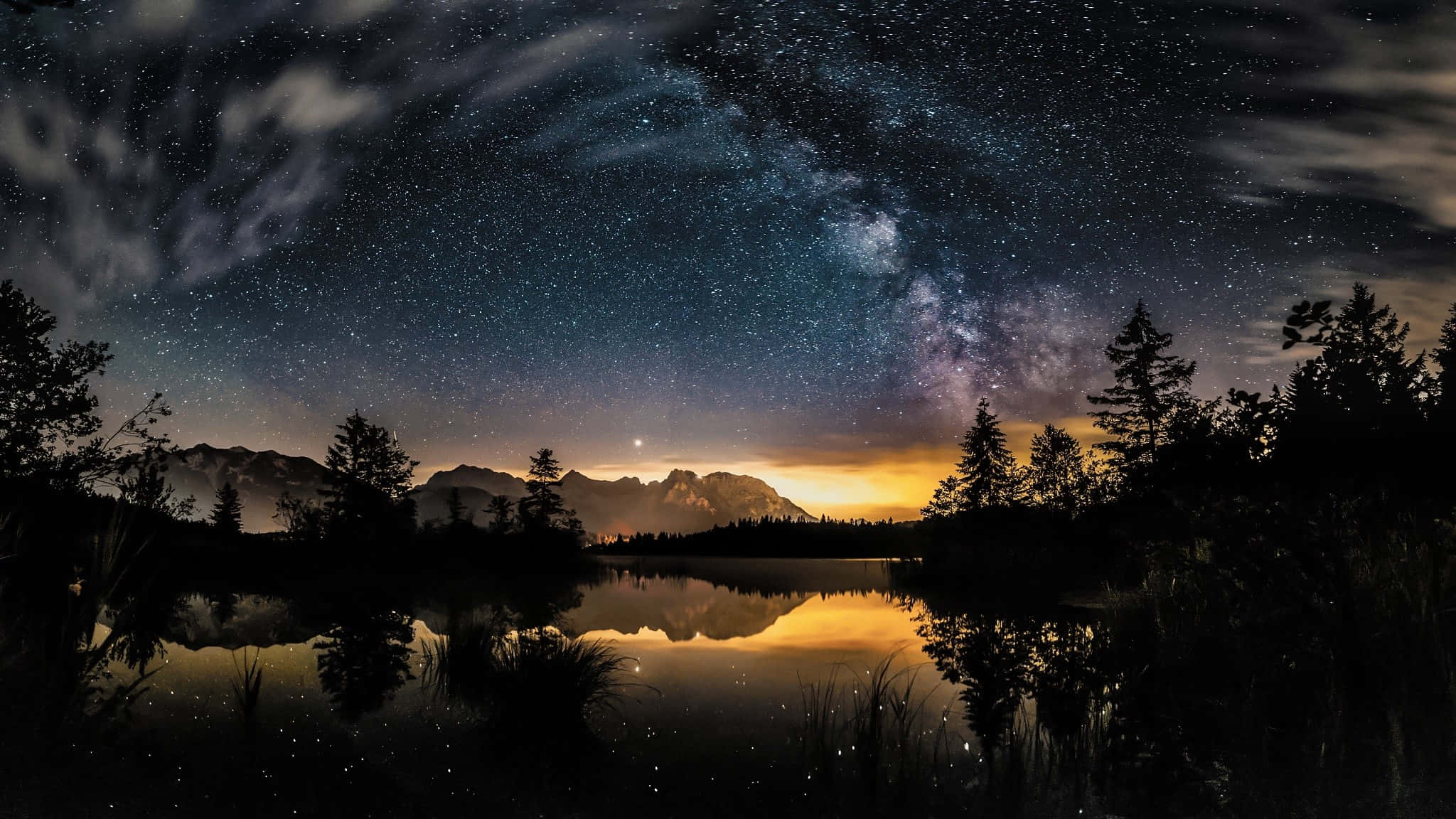 Dark Sky 桌布 壁紙 — 繁星點點的夜空，銀河拱起，映照在平靜湖面上的山脈和樹木剪影。