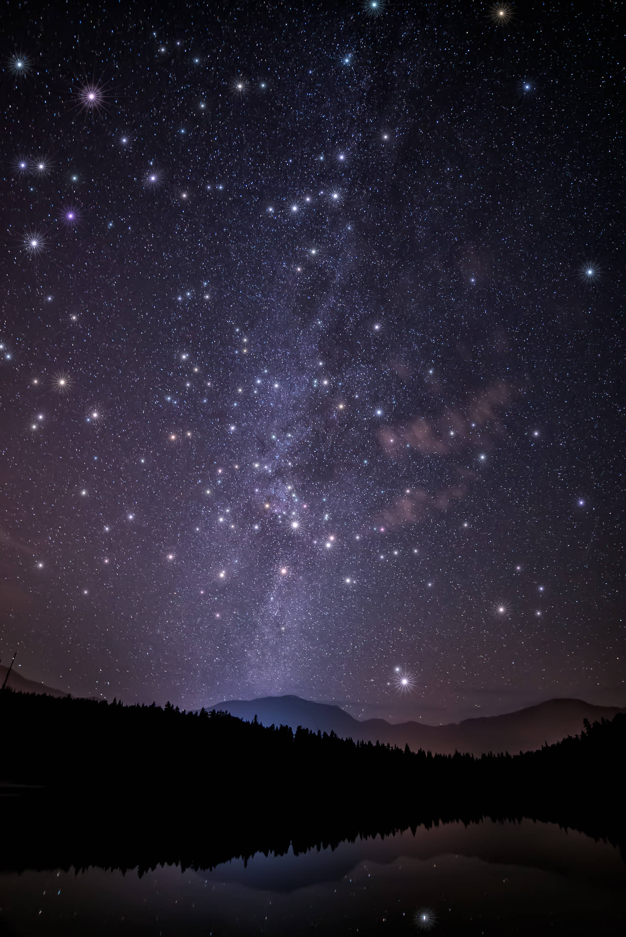 銀河 桌布 壁紙 — 繁星點點的夜空，銀河拱起在剪影山脈和寧靜的湖面上，倒映著天體景象。