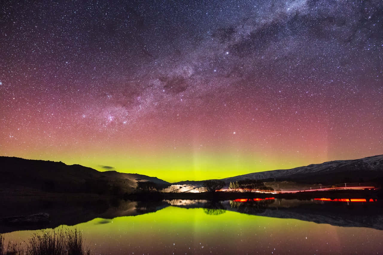 Southern Lights 桌布 壁紙 — 繁星點點的夜空，銀河拱起在平靜的湖面上，倒映出鮮豔的綠色極光和遙遠的紅色光跡。