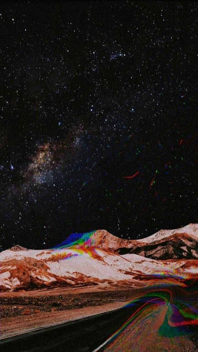 美學 iPhone 壁紙 桌布 壁紙 — 繁星點點的夜空，銀河拱起在積雪的山峰和蜿蜒的道路之上，兩者都閃爍著彩虹般的色彩。