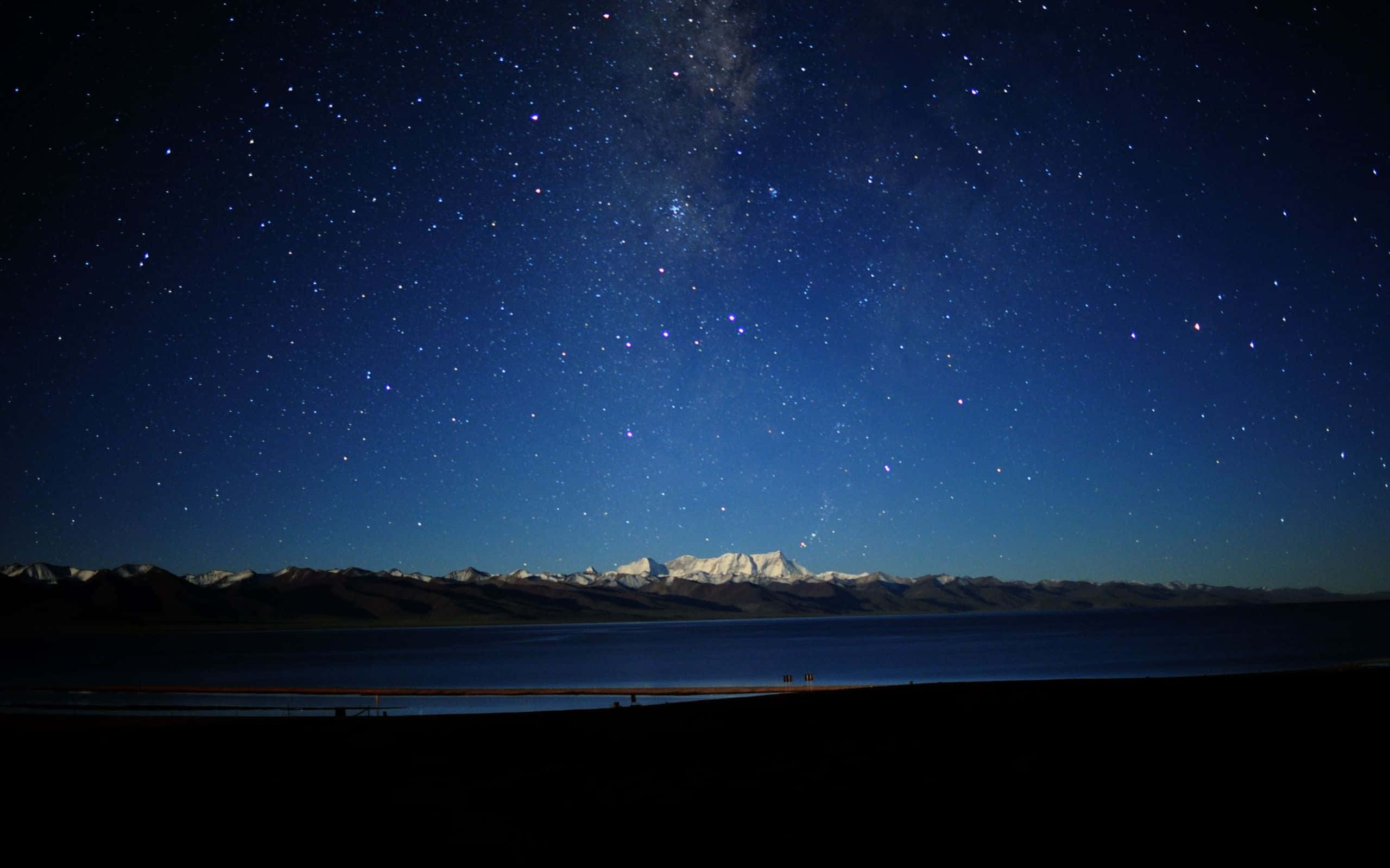 Stars 桌布 壁紙 — 繁星點點的夜空，銀河拱跨在平靜的湖泊和積雪覆蓋的山脈之上。