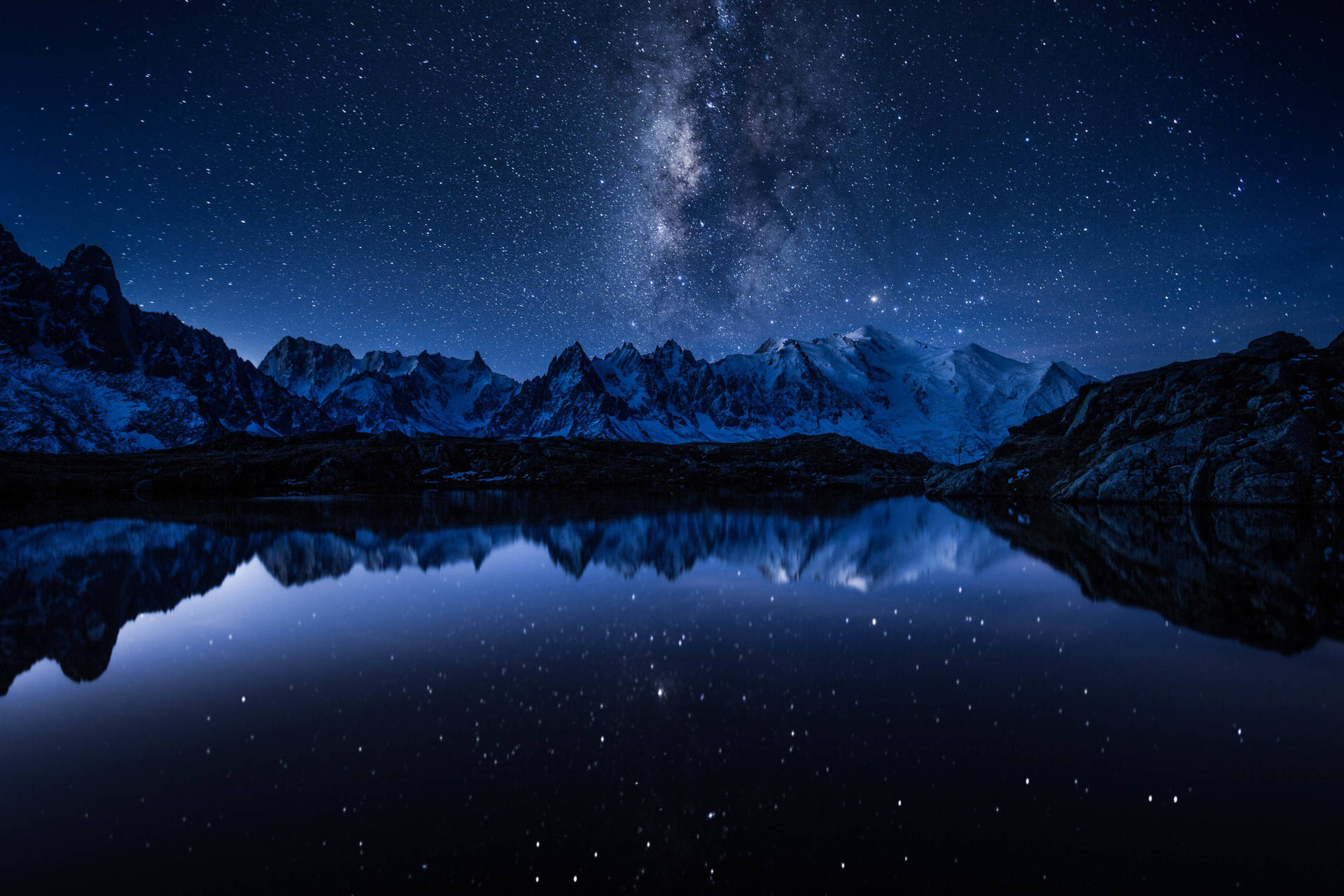 星空下積雪的山巒，夜晚倒映在平靜的湖面。 — 5K 壁紙
