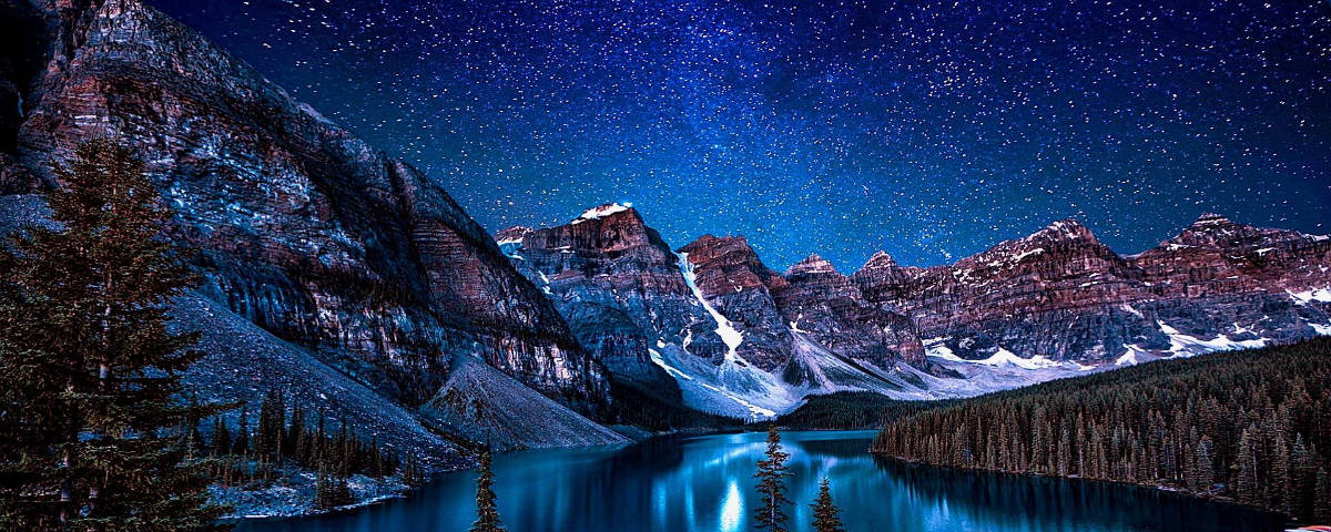 Starry Sky 桌布 壁紙 — 繁星點點的夜空倒映在寧靜的山間湖泊中，四周環繞著白雪覆蓋的山峰和常綠樹木。