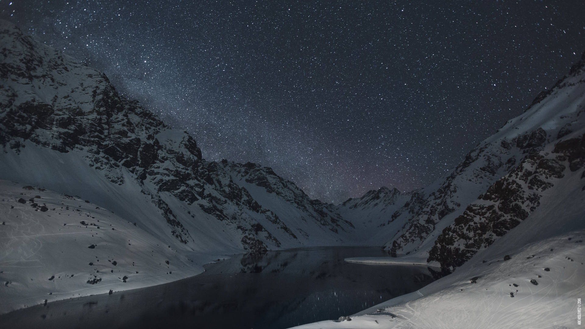 雪山環繞著寧靜湖泊中倒映的繁星夜空。 — 5K 壁紙