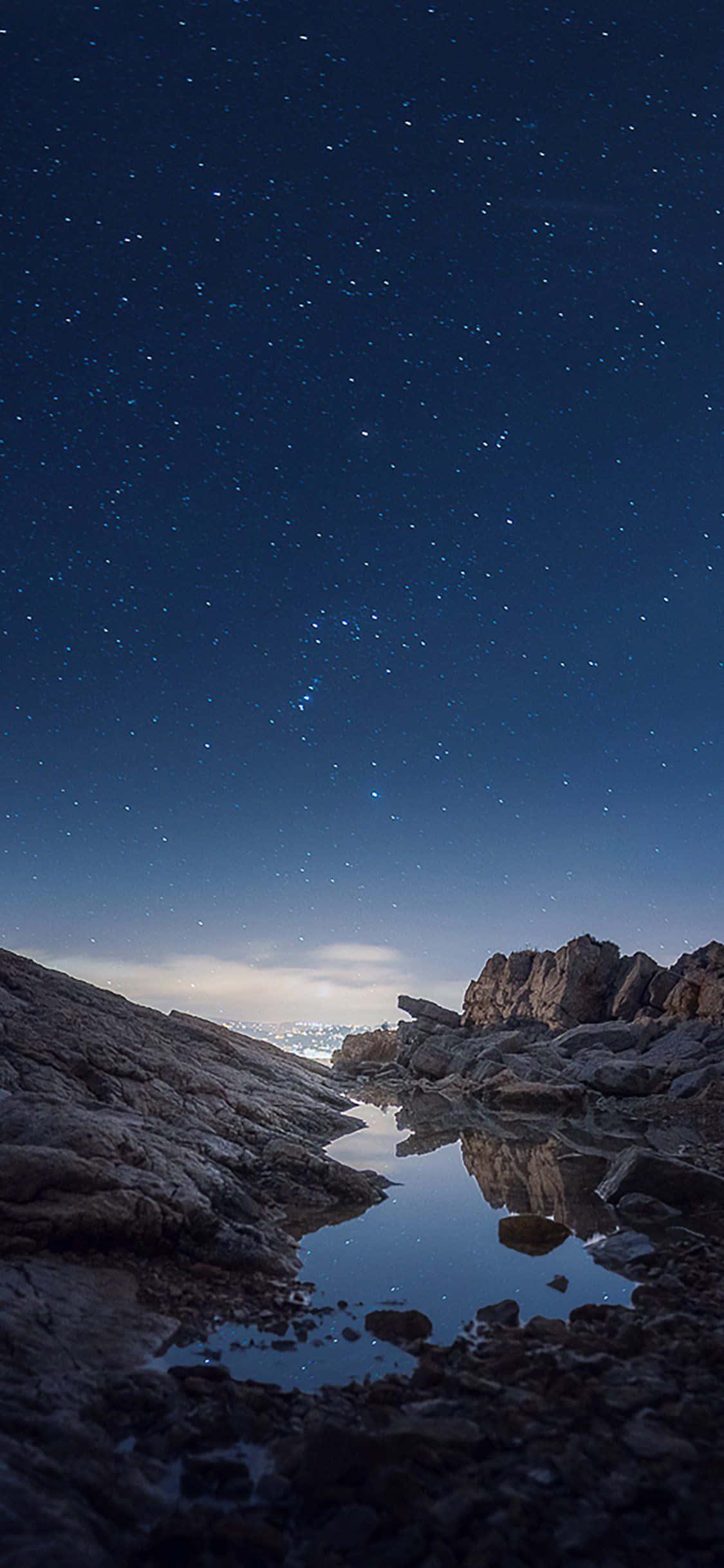 iPhone X Nature 桌布 壁紙 — 繁星點點的夜空倒映在崎嶇岩石地形中的一池平靜水面上。