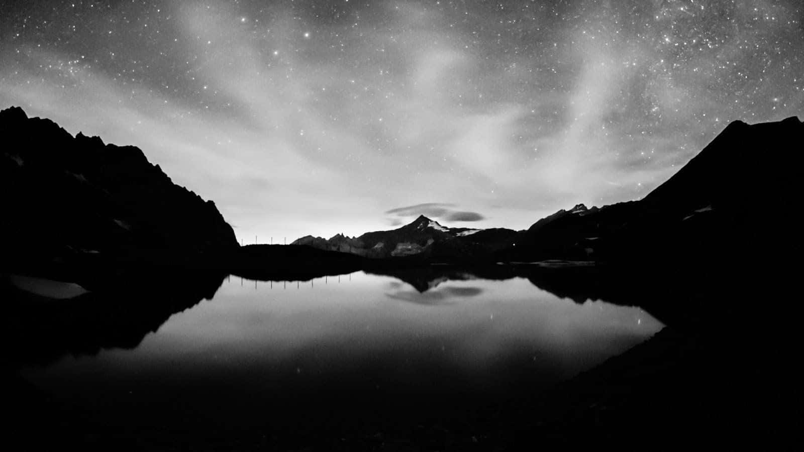 黑白 桌布 壁紙 — 繁星點點的夜空完美地倒映在平靜的山間湖面上，四周環繞著黑暗的山峰剪影。